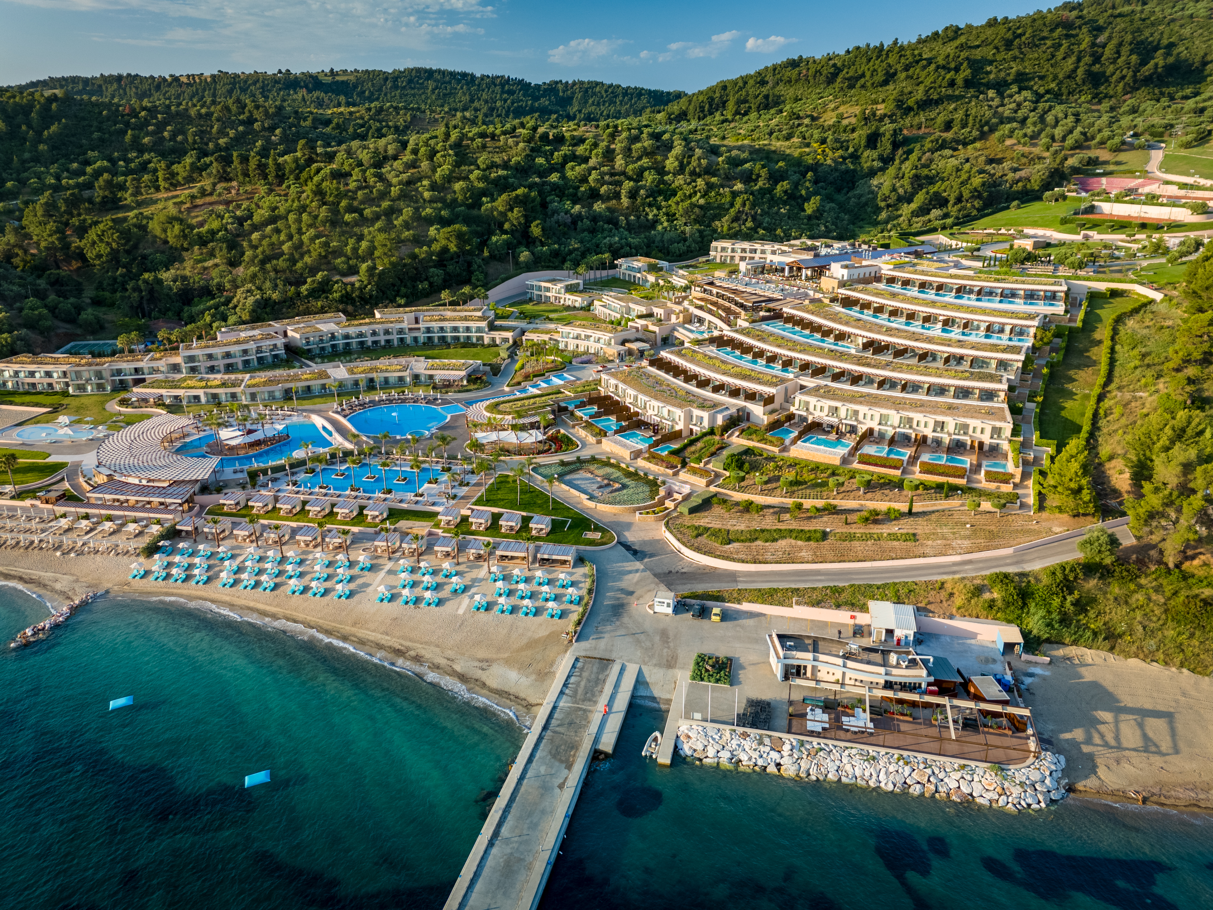 Aerial view of Miraggio Thermal Spa Resort featuring tiered architecture, turquoise pools, and a private beachfront