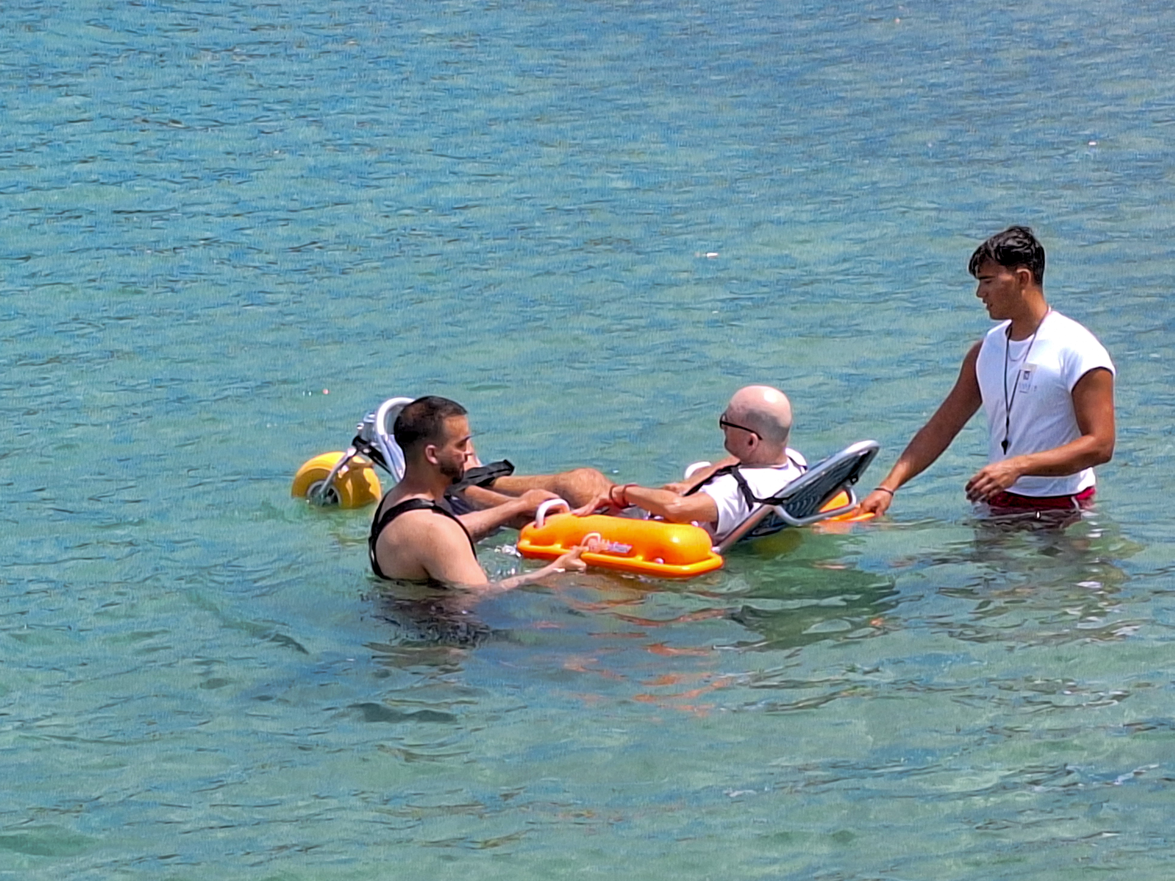 Lifeguards assisting guest using a floating beach wheelchair for safe access