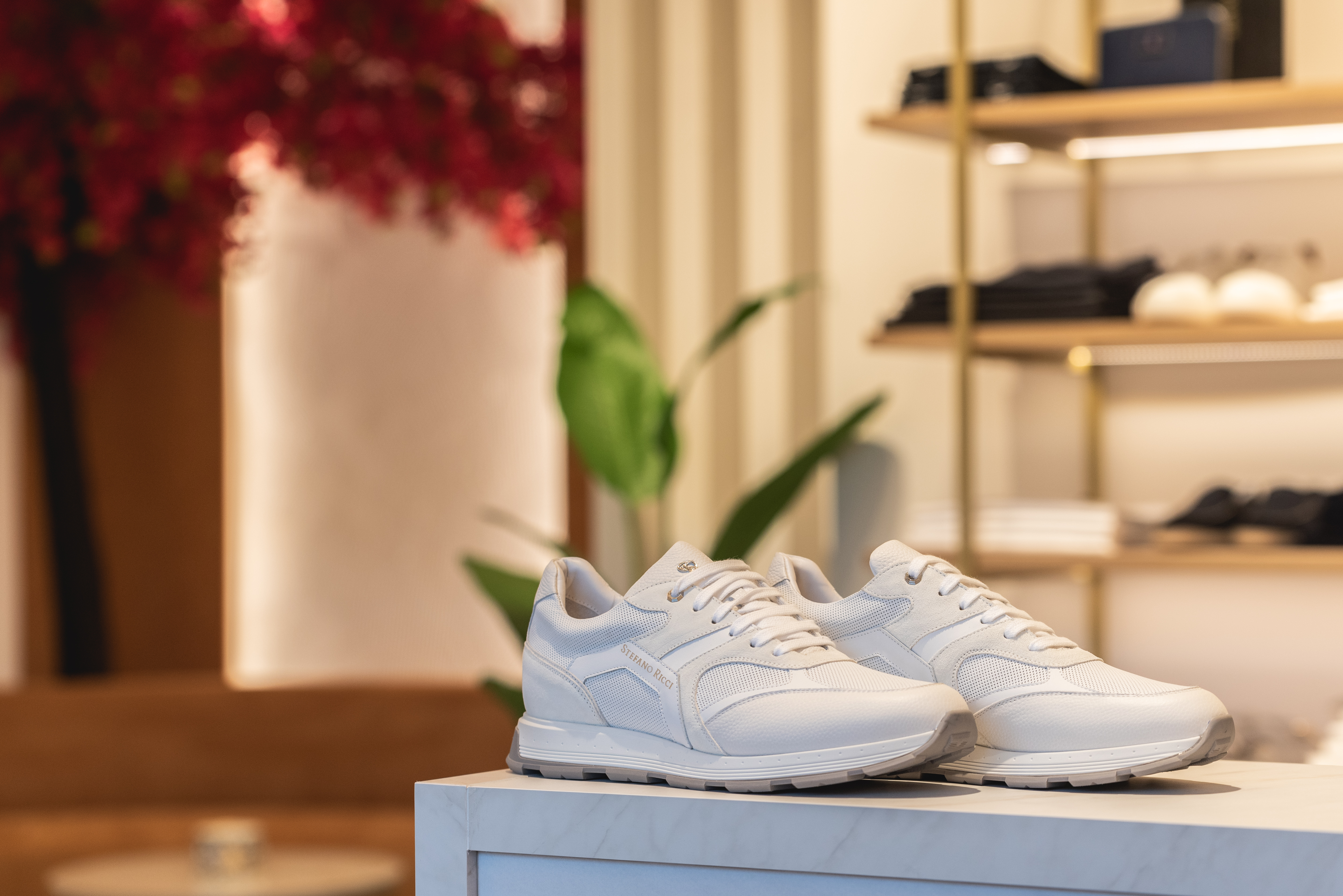 White Stefano Ricci sneakers displayed on marble counter with boutique interior in the background