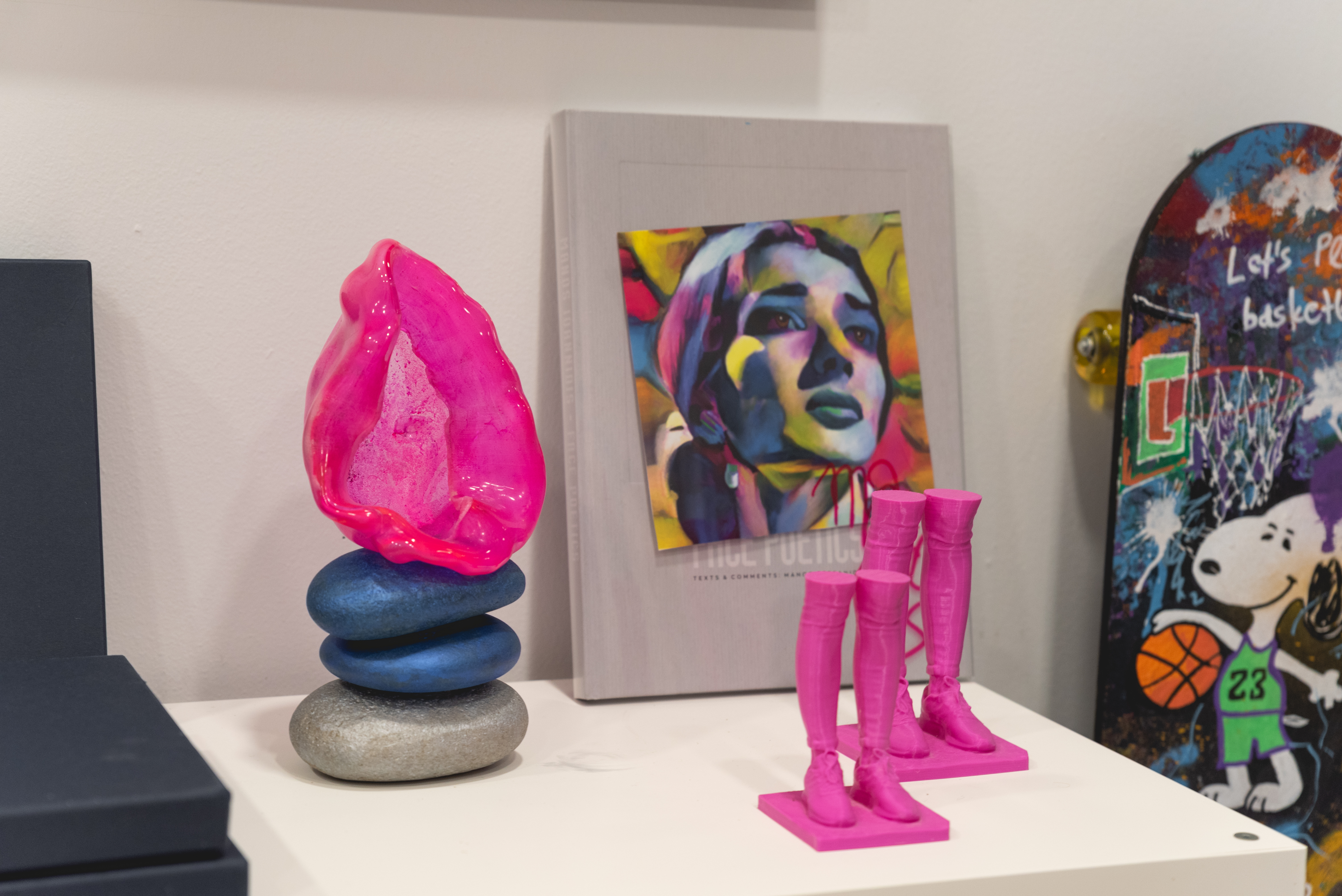 Close up of pebble sculpture with pink accents and two pink boots figurines in front of artworks