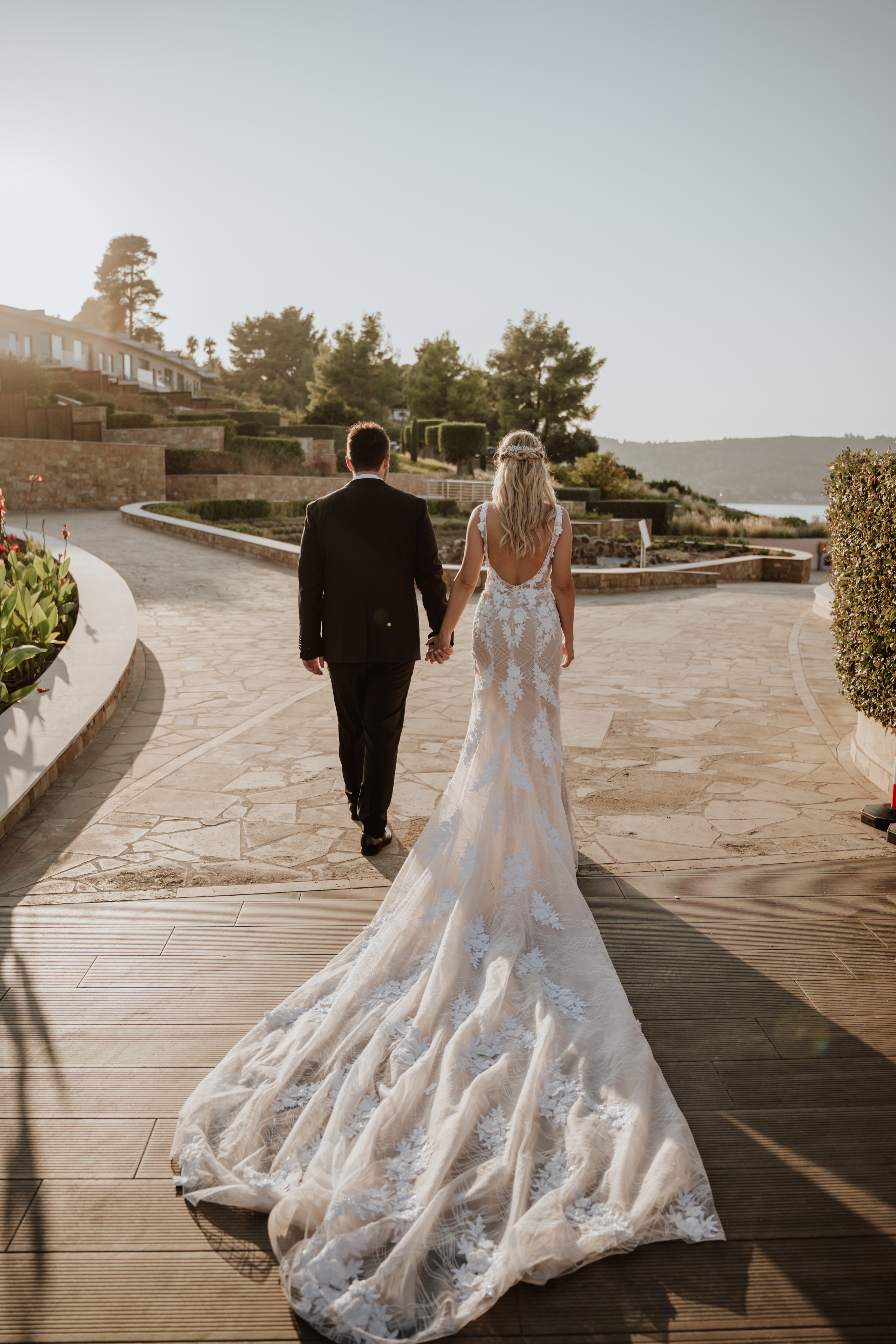 Bride and groom walking hand in hand at sunset with elegant wedding gown train