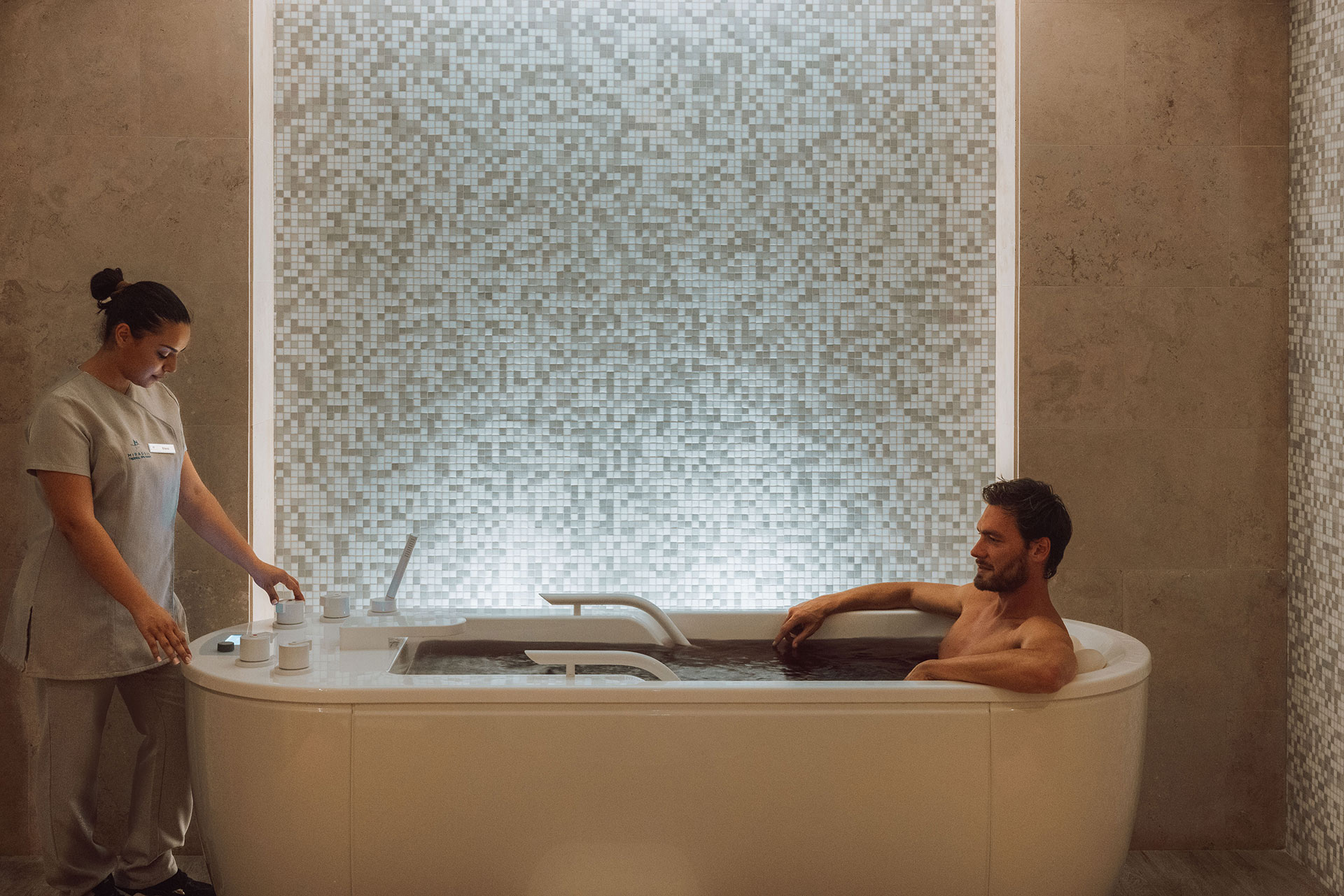 Guest enjoying therapeutic hydrotherapy bath assisted by spa therapist