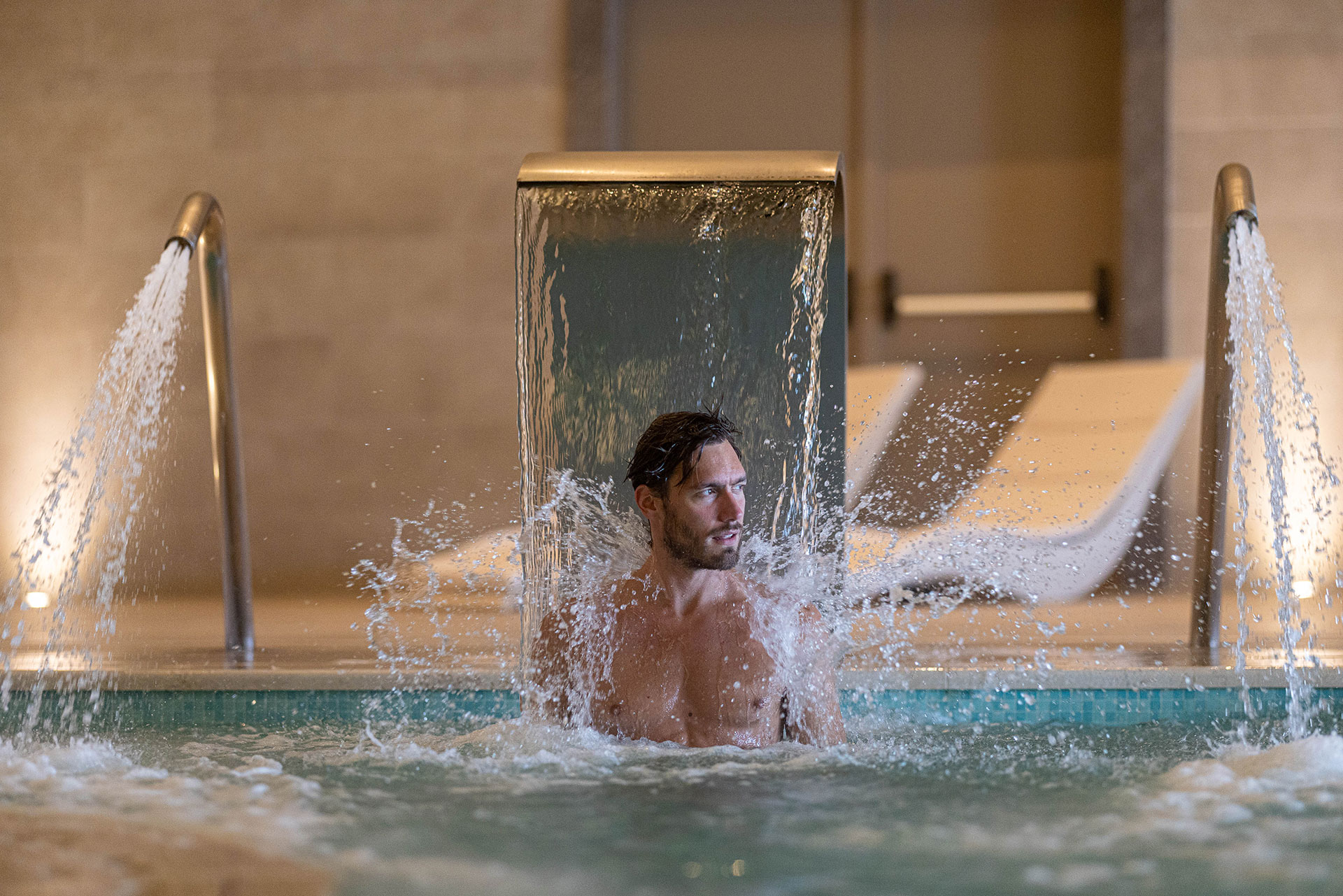 Man enjoying neck massage jet under water cascade at indoor thermal spa pool