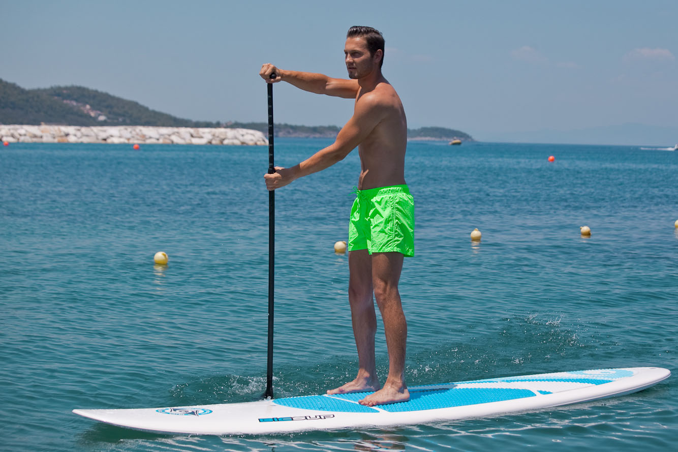 Man paddleboarding on calm turquoise sea under clear blue sky