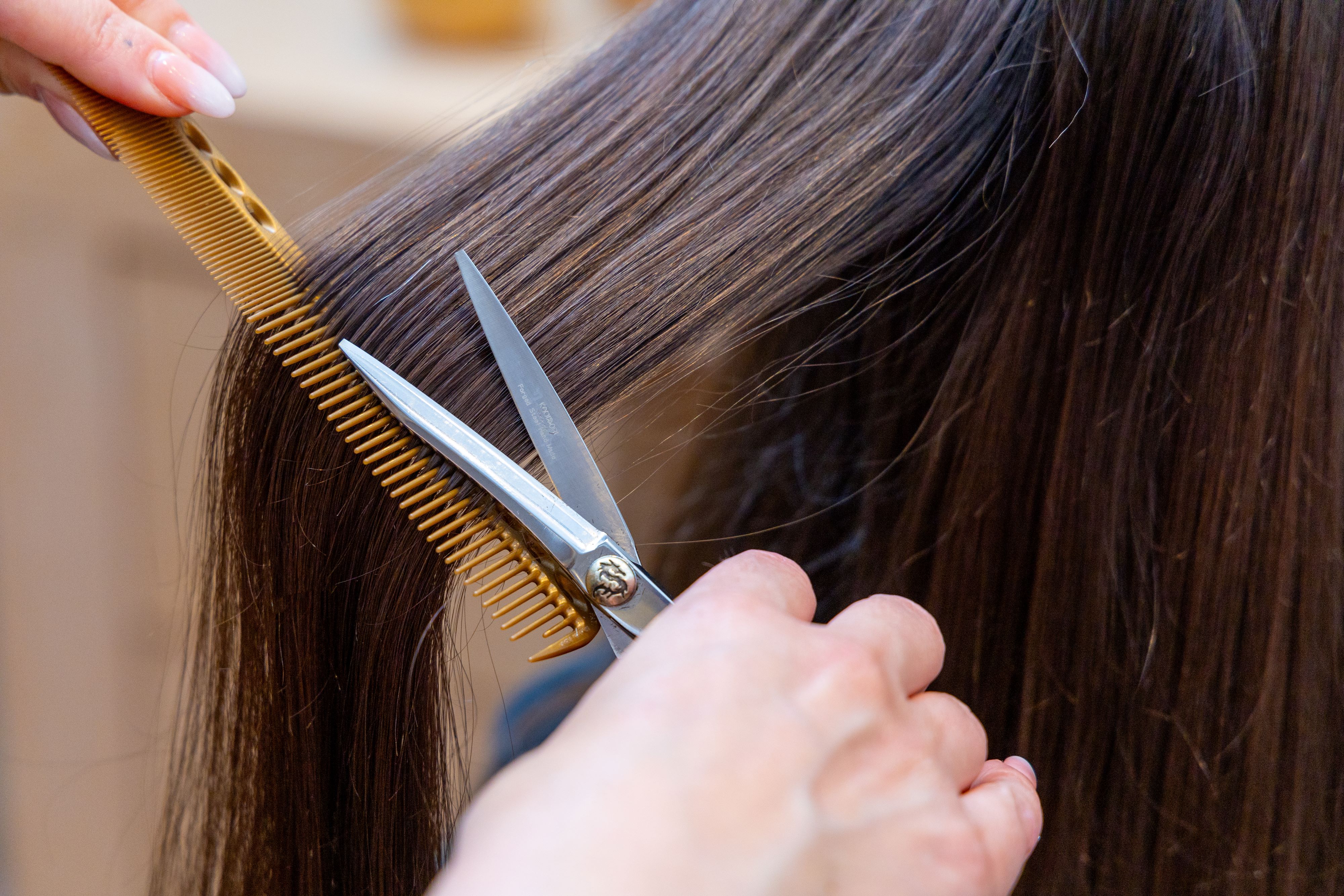 Close up of stylist cutting long brown hair with precision scissors