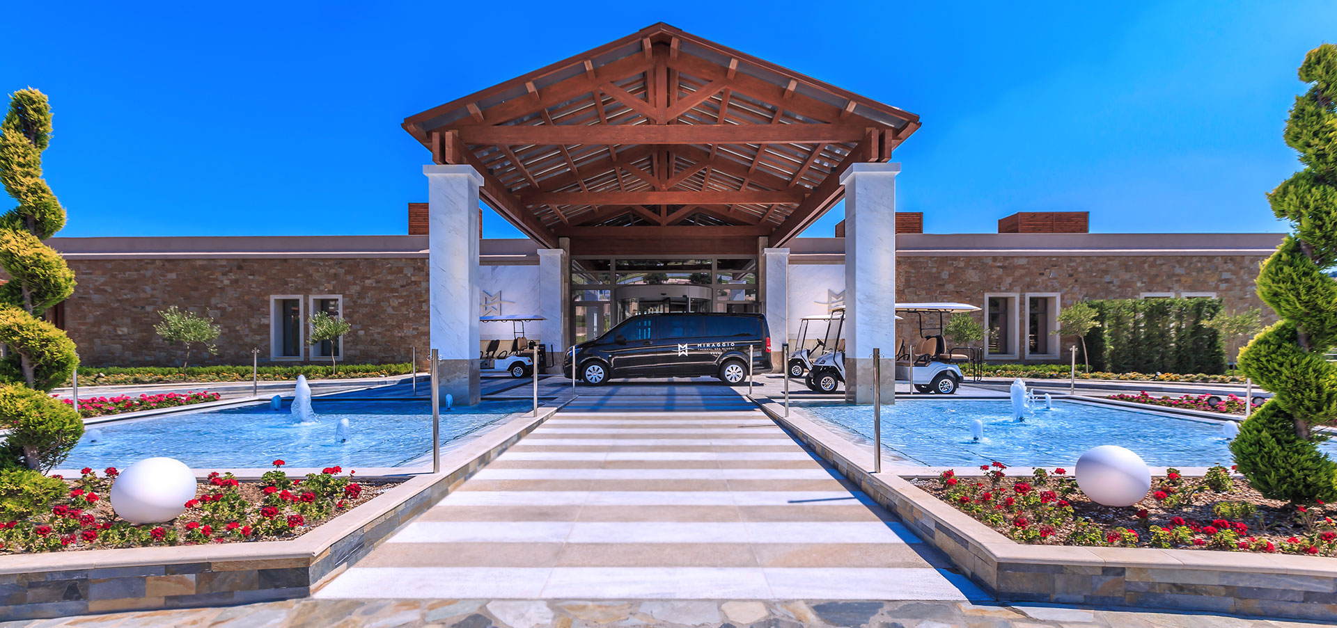 Miraggio Resort entrance with marble pillars, water fountains, and luxury transfer vehicles