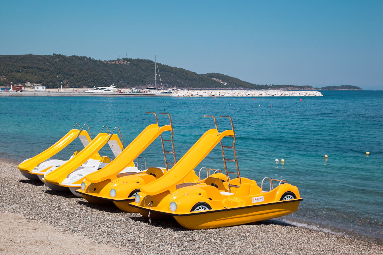 Yellow pedal boats with slides lined up on the beach by the turquoise sea
