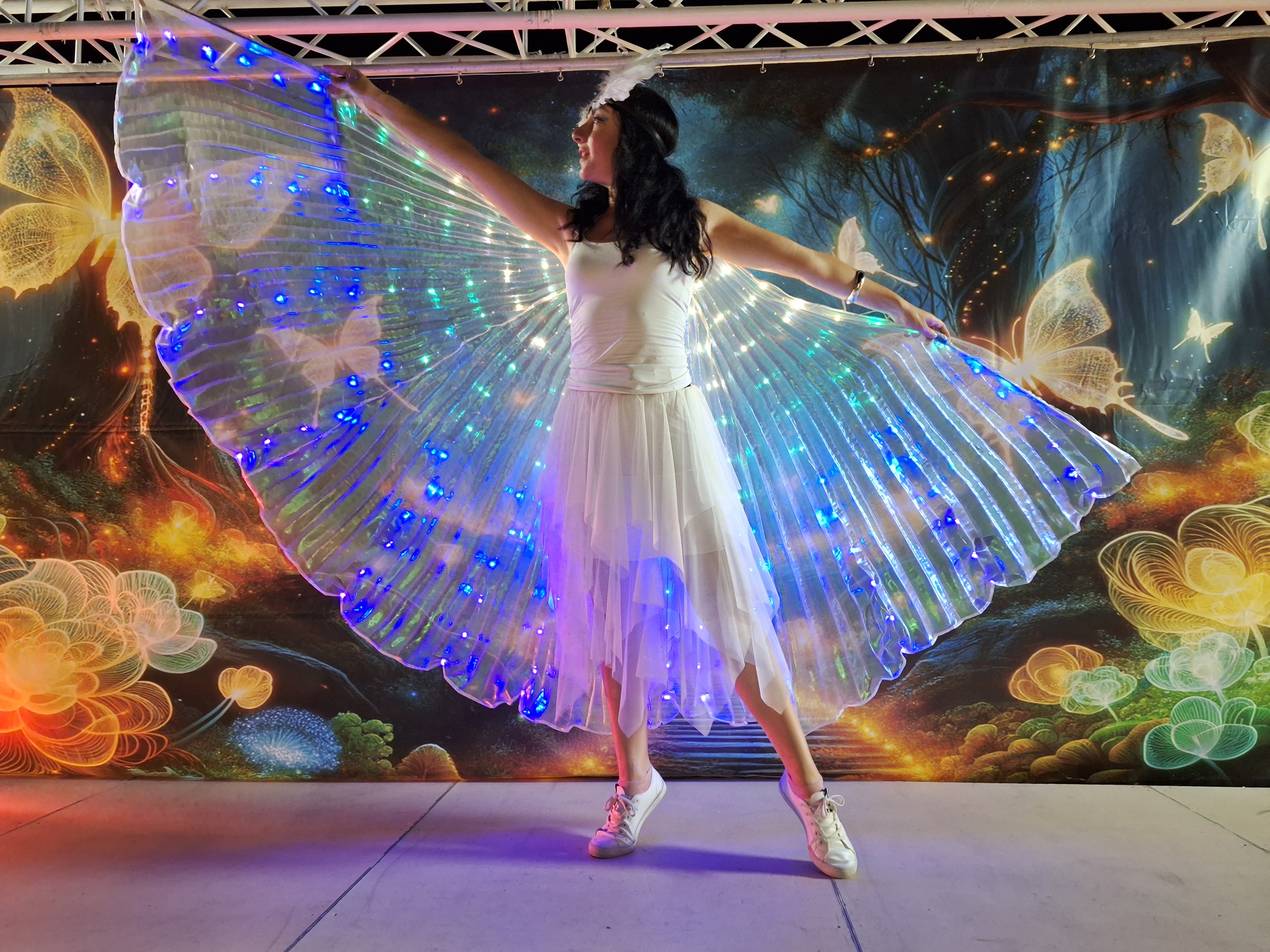 Performer in glowing fairy costume with illuminated wings during evening show