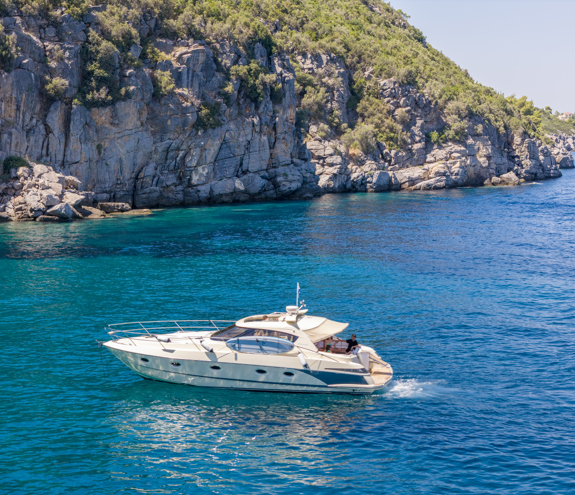 Luxury motor yacht cruising along turquoise waters beside rocky cliffs covered in greenery