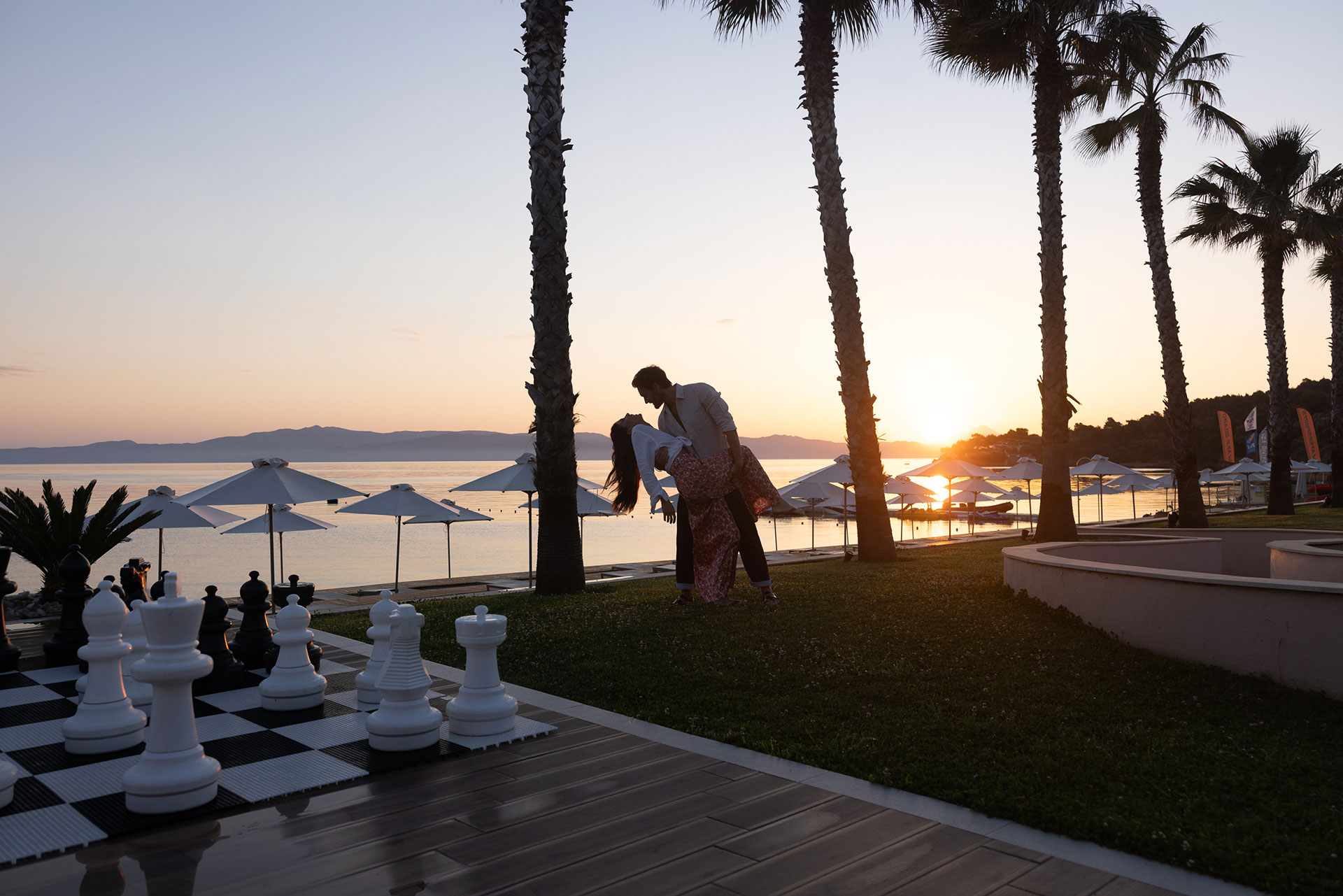 Romantic couple dancing by seaside giant chessboard at sunset