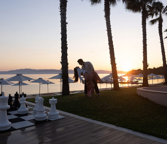 Romantic couple dancing by seaside giant chessboard at sunset