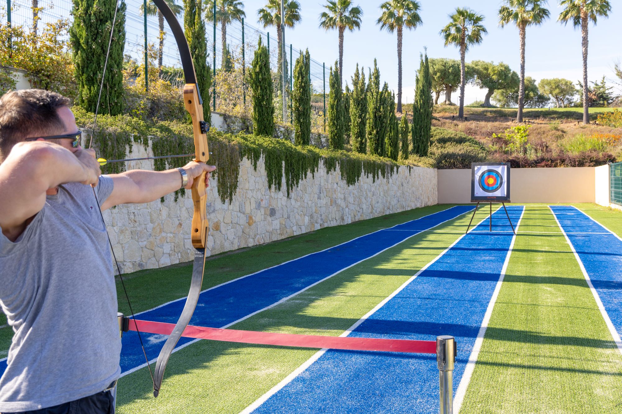 Man practicing archery on outdoor shooting range surrounded by palm trees