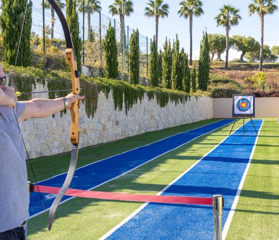Man practicing archery on outdoor shooting range surrounded by palm trees