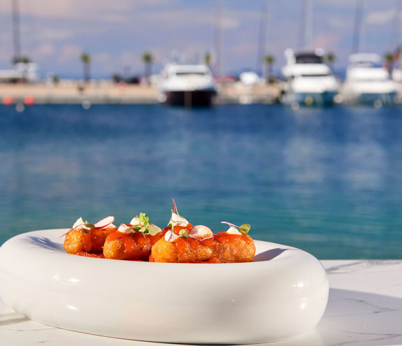 Elegant seafood croquettes garnished with radish and herbs, served with a marina view