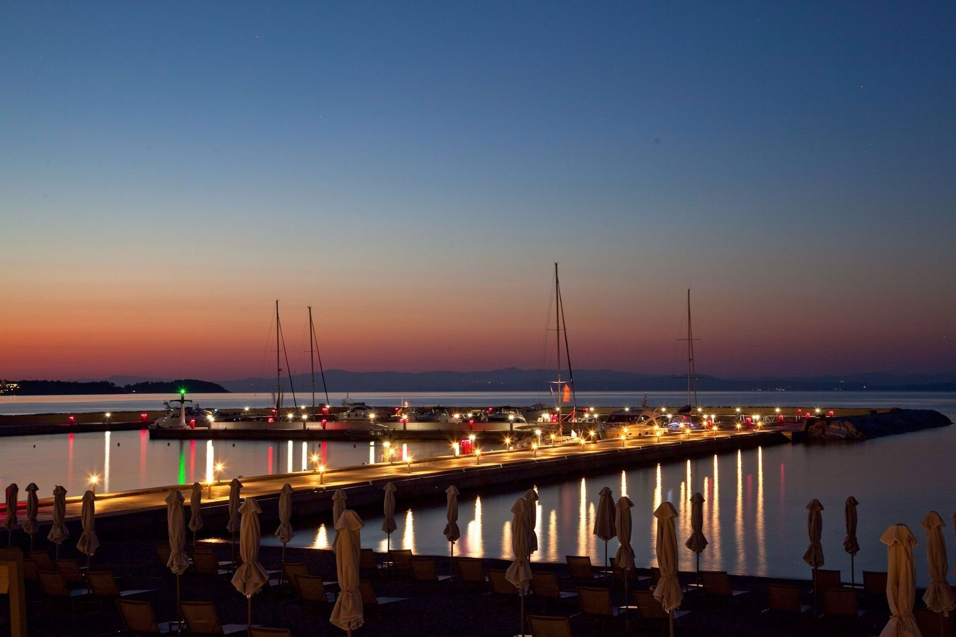 Scenic evening view of the illuminated marina with yachts and calm sea at sunset