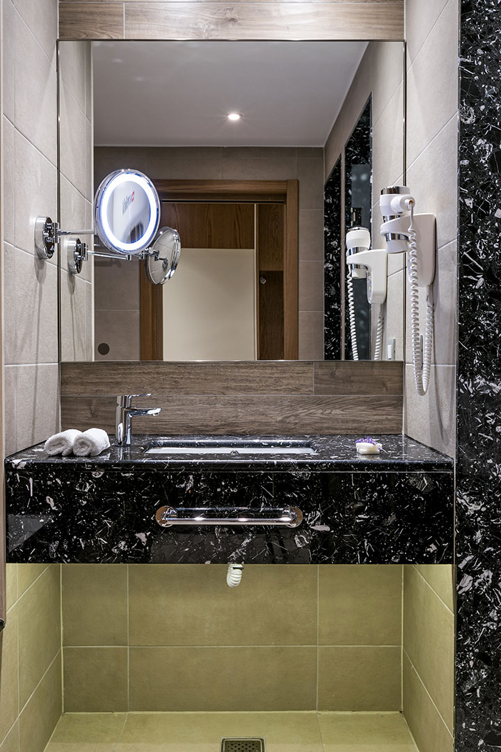 Elegant deluxe room's bathroom with marble walls and countertop featuring vanity mirror