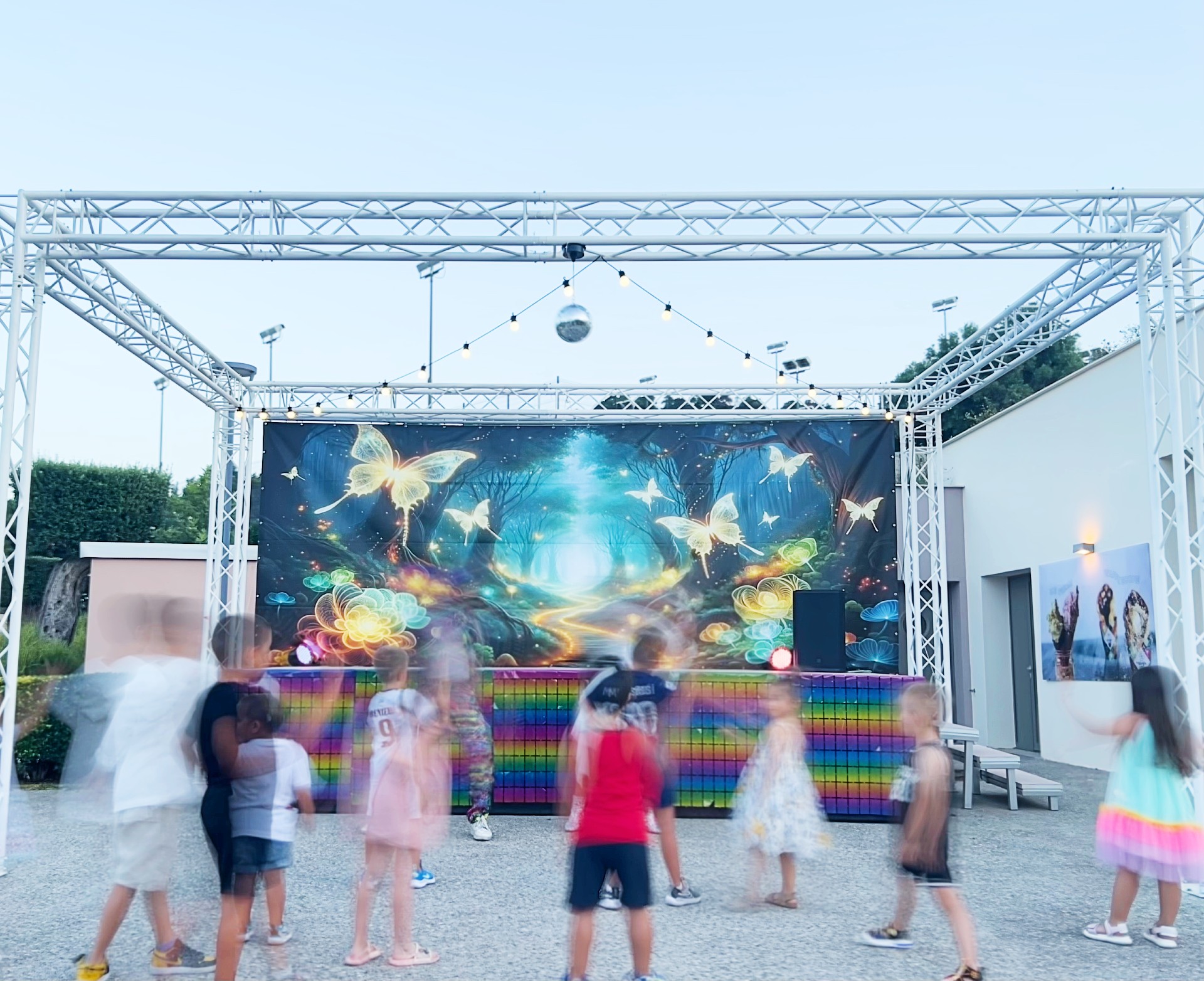 Children dancing at an outdoor evening event with colorful lights and fairy backdrop