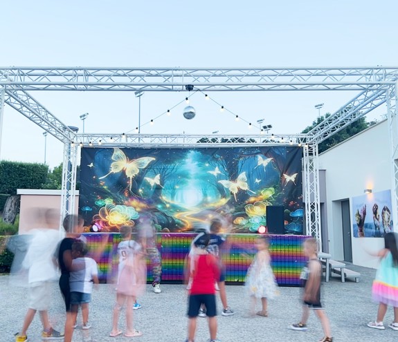 Children dancing at an outdoor evening event with colorful lights and fairy backdrop