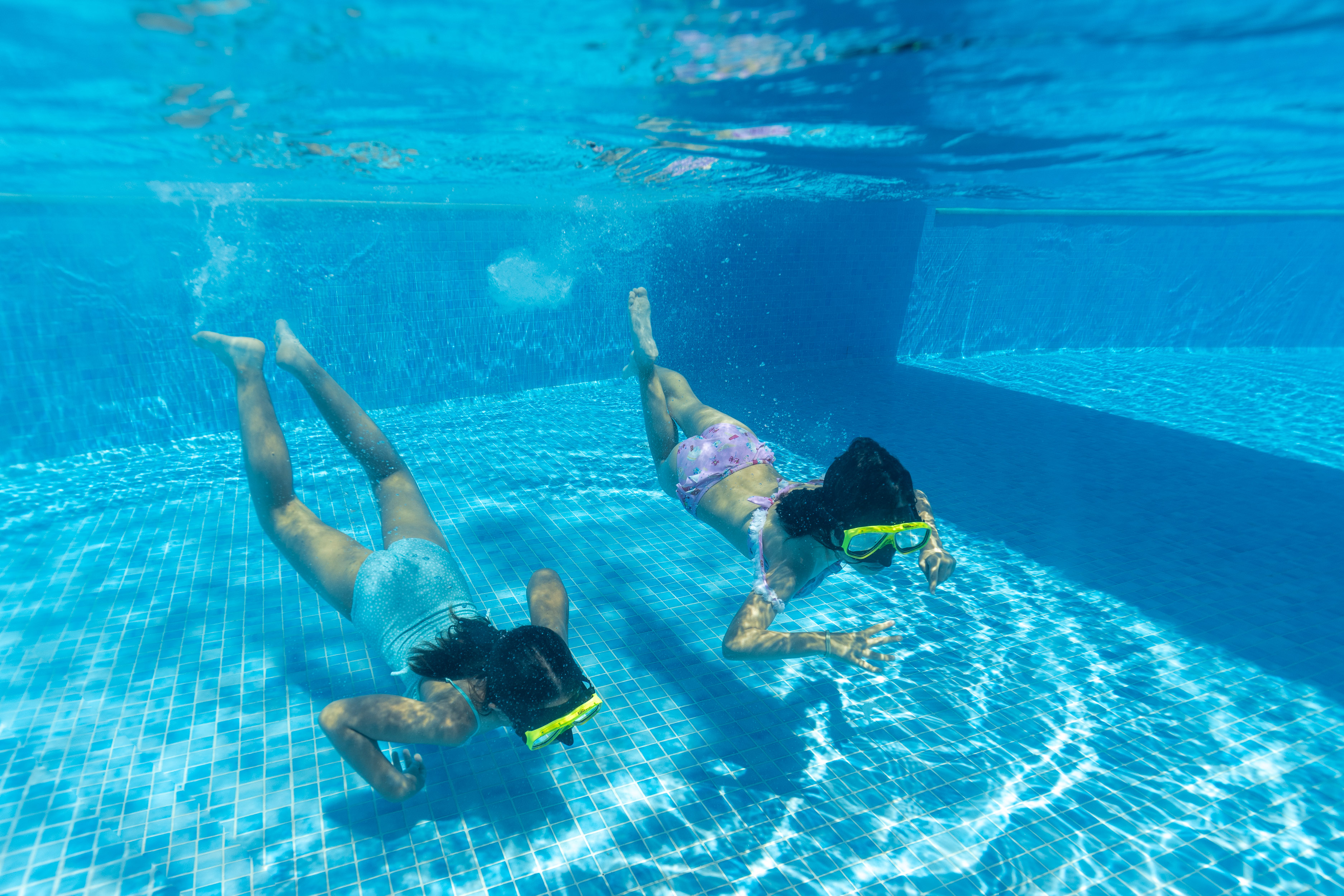 Two children swimming underwater with masks in a bright pool