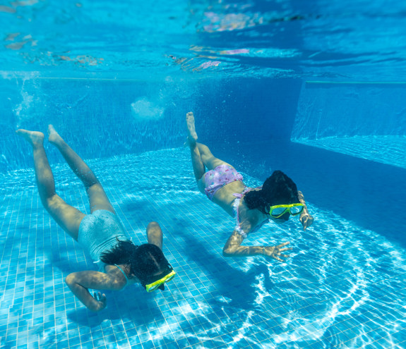 Two children swimming underwater with masks in a bright pool