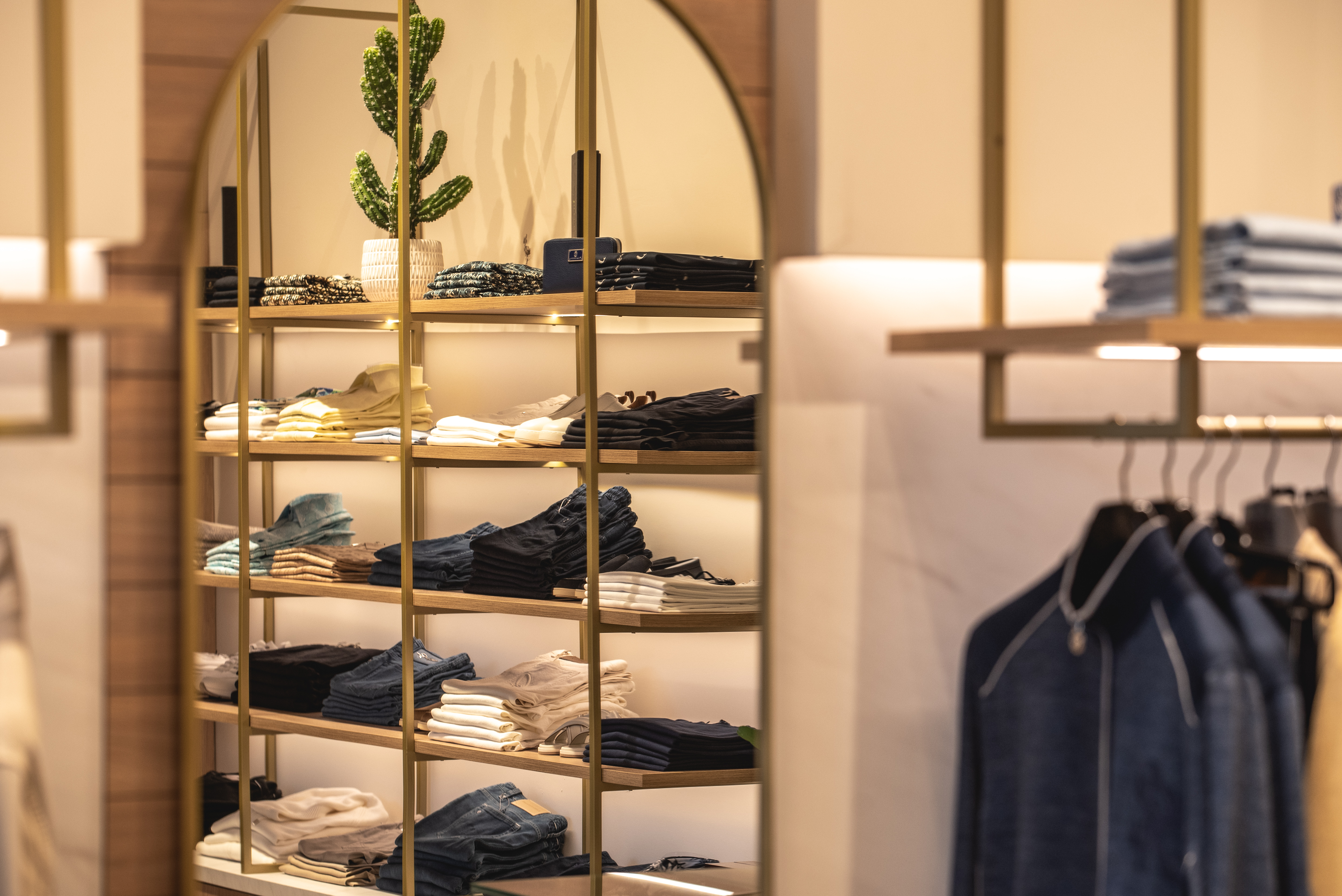 Interior of boutique with stacked men's clothing on elegant wooden shelves with gold accents