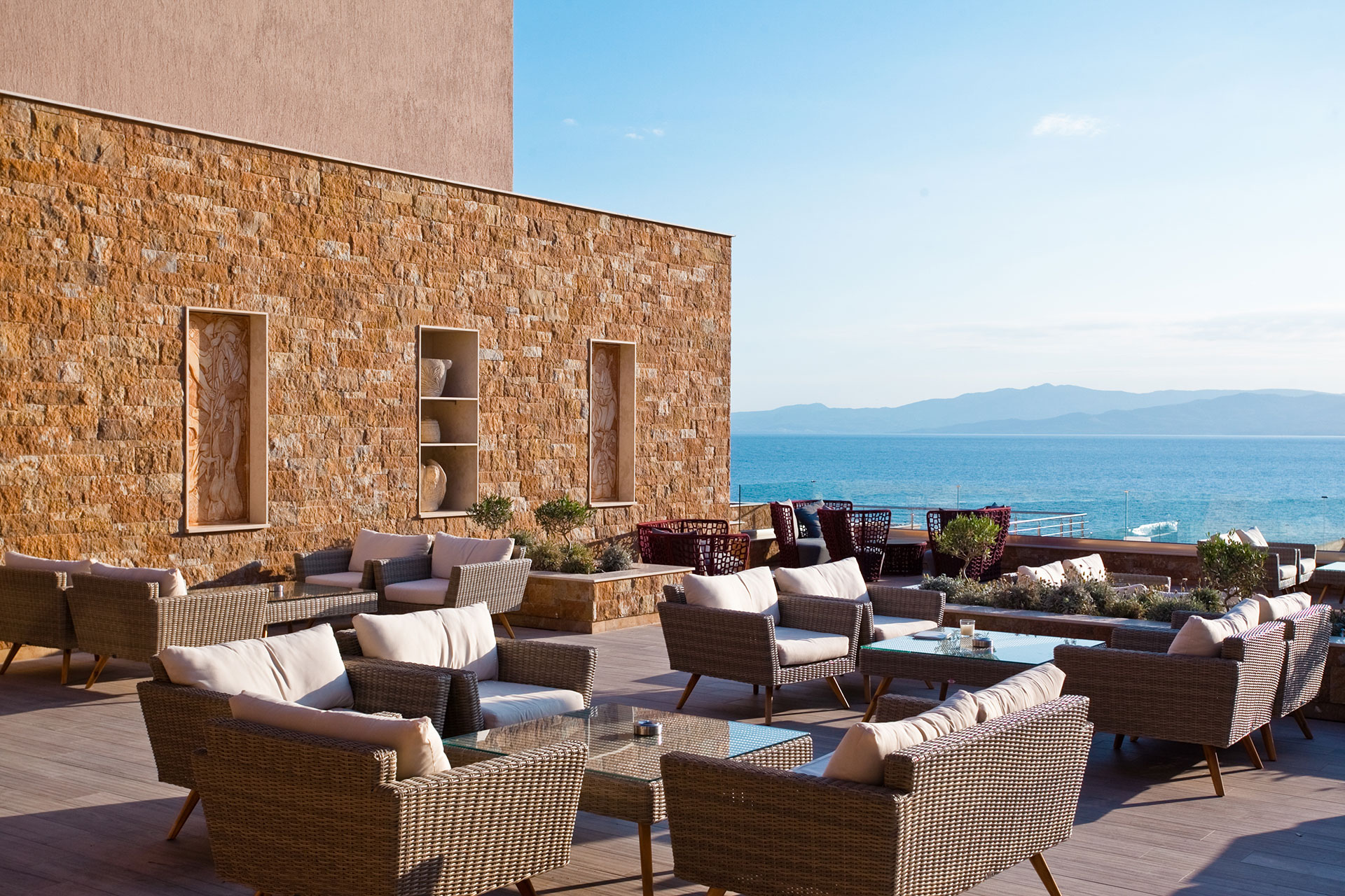 Elegant terrace seating with panoramic sea view and stone wall backdrop at Lobby bar