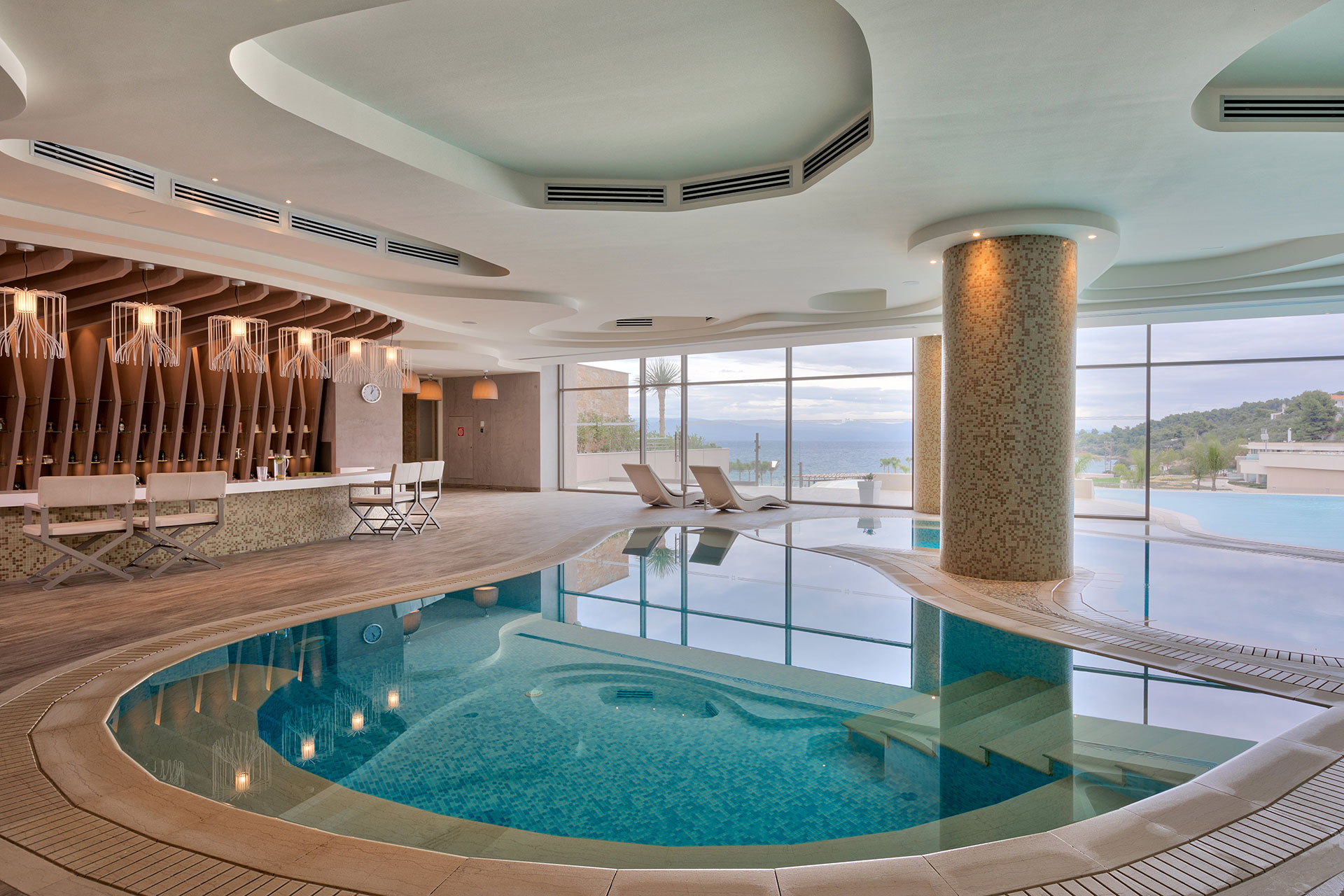 Indoor thermal pool with elegant lighting, sea views, and modern bar area