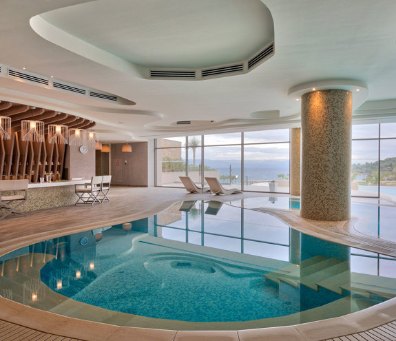 Indoor thermal pool with elegant lighting, sea views, and modern bar area