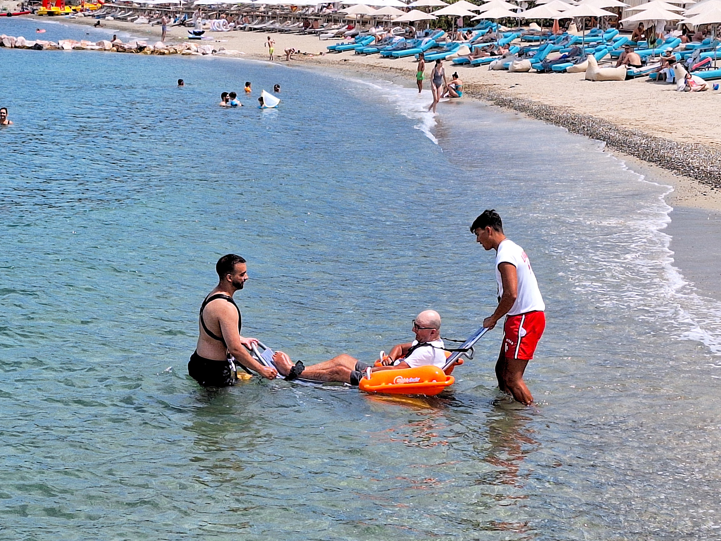 Assisted sea access for guest with mobility needs, supported by lifeguards at the beach