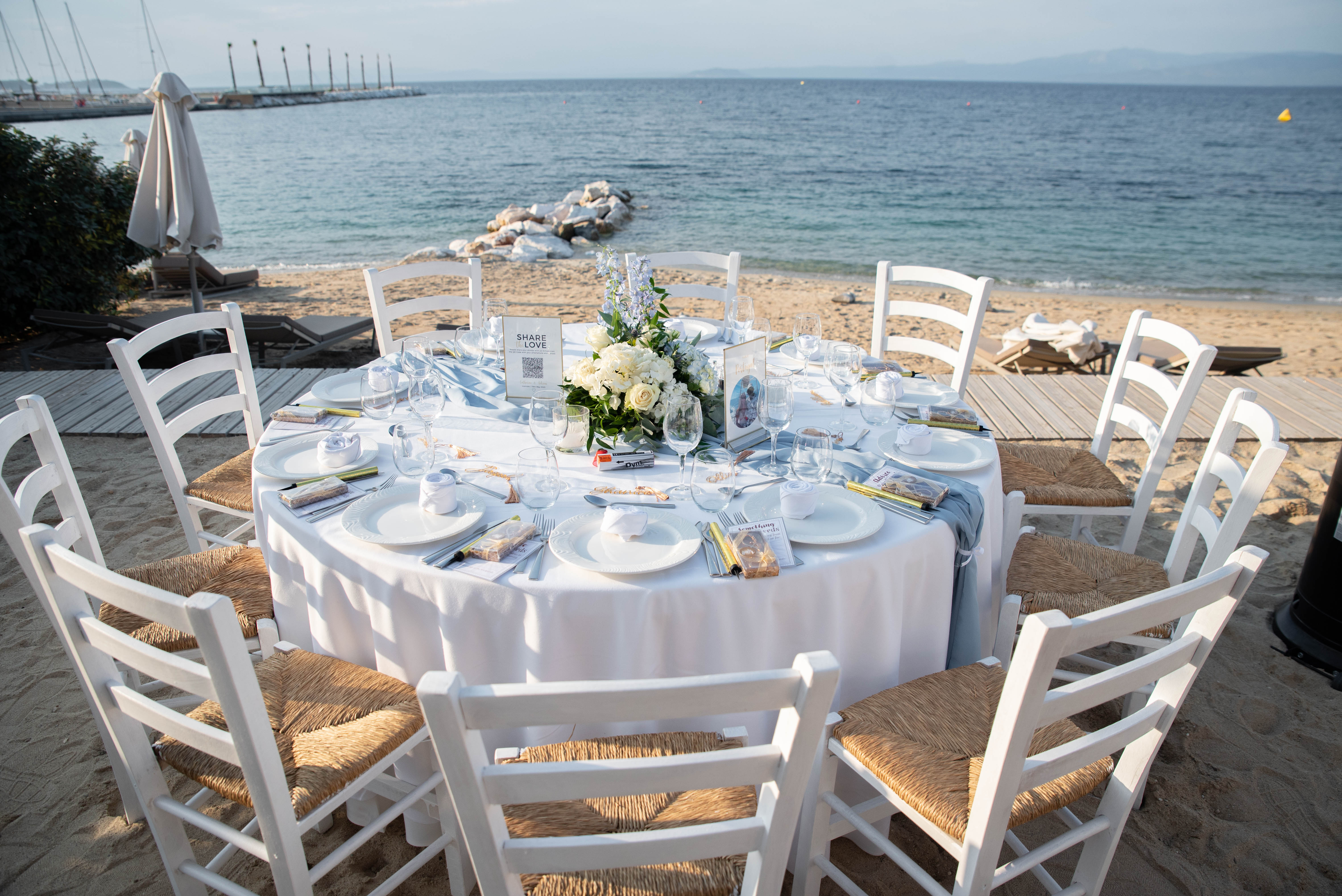 Elegant wedding setup on the beach with rustic chairs, and round table with floral design 