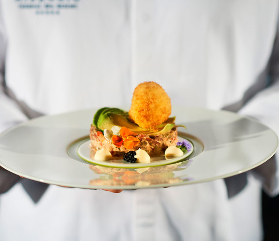 Chef presenting tuna tartare with avocado slices, crispy egg, and edible flowers