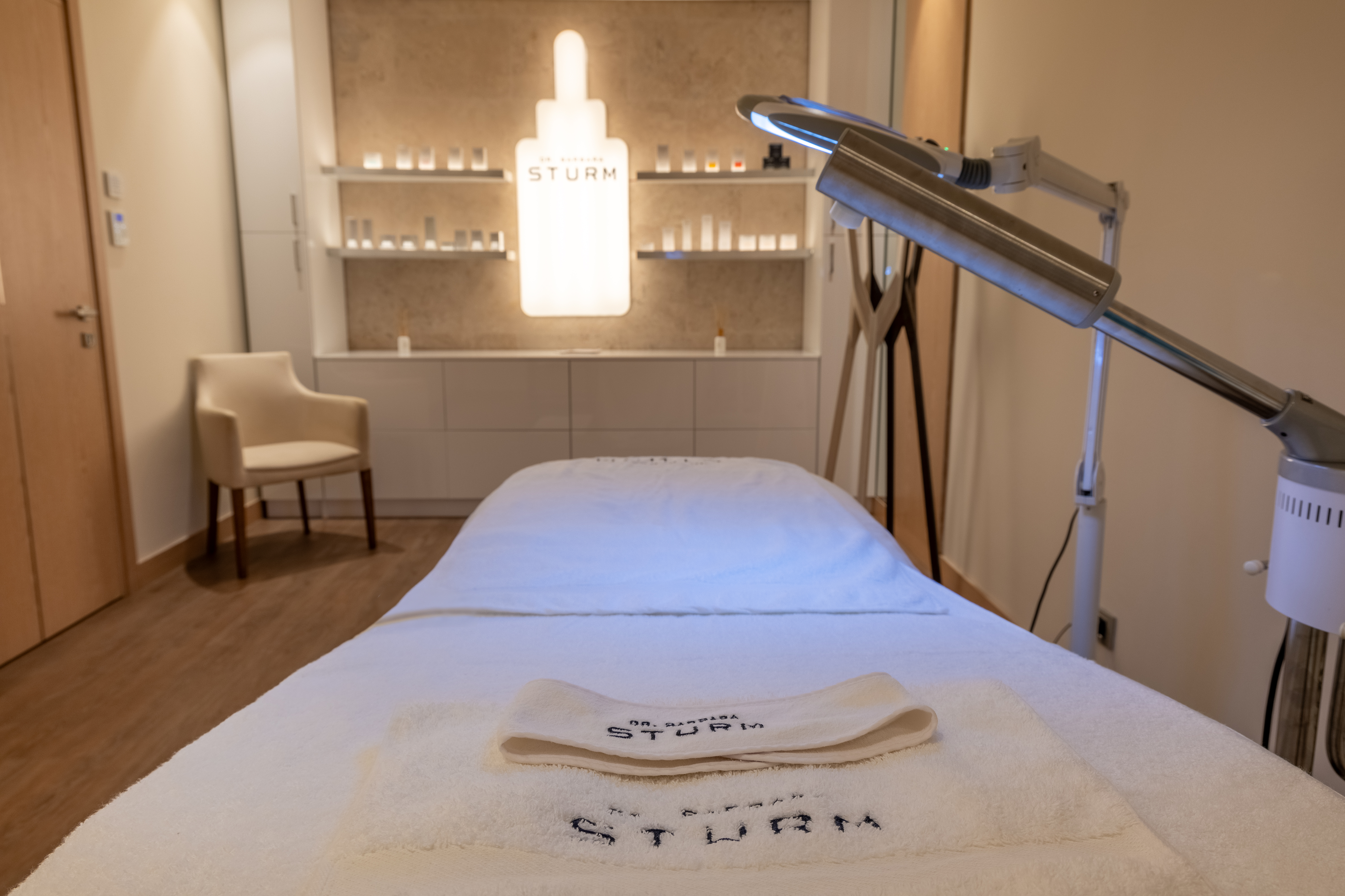 Spa treatment room with warm ambient lighting, plush treatment bed, and shelves of premium skincare products