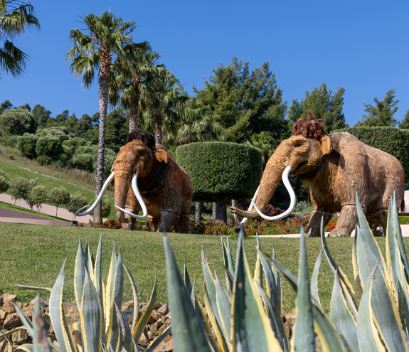 Life-sized wooly mammoth sculptures surrounded by palm trees and greenery