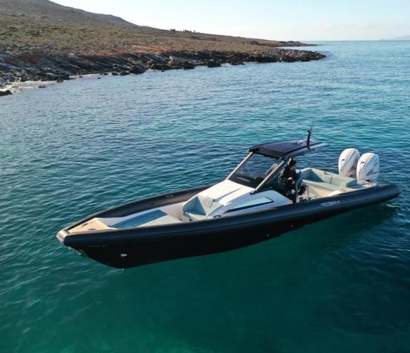 Modern black RIB with twin outboards cruising over clear turquoise water near a rocky shoreline