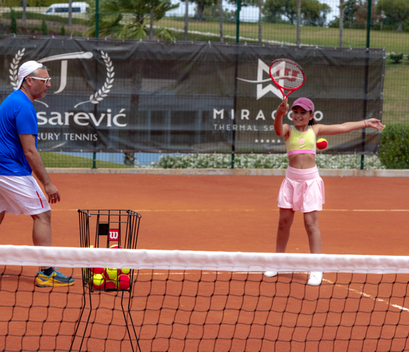 Girl practicing tennis with coach on clay court during training session