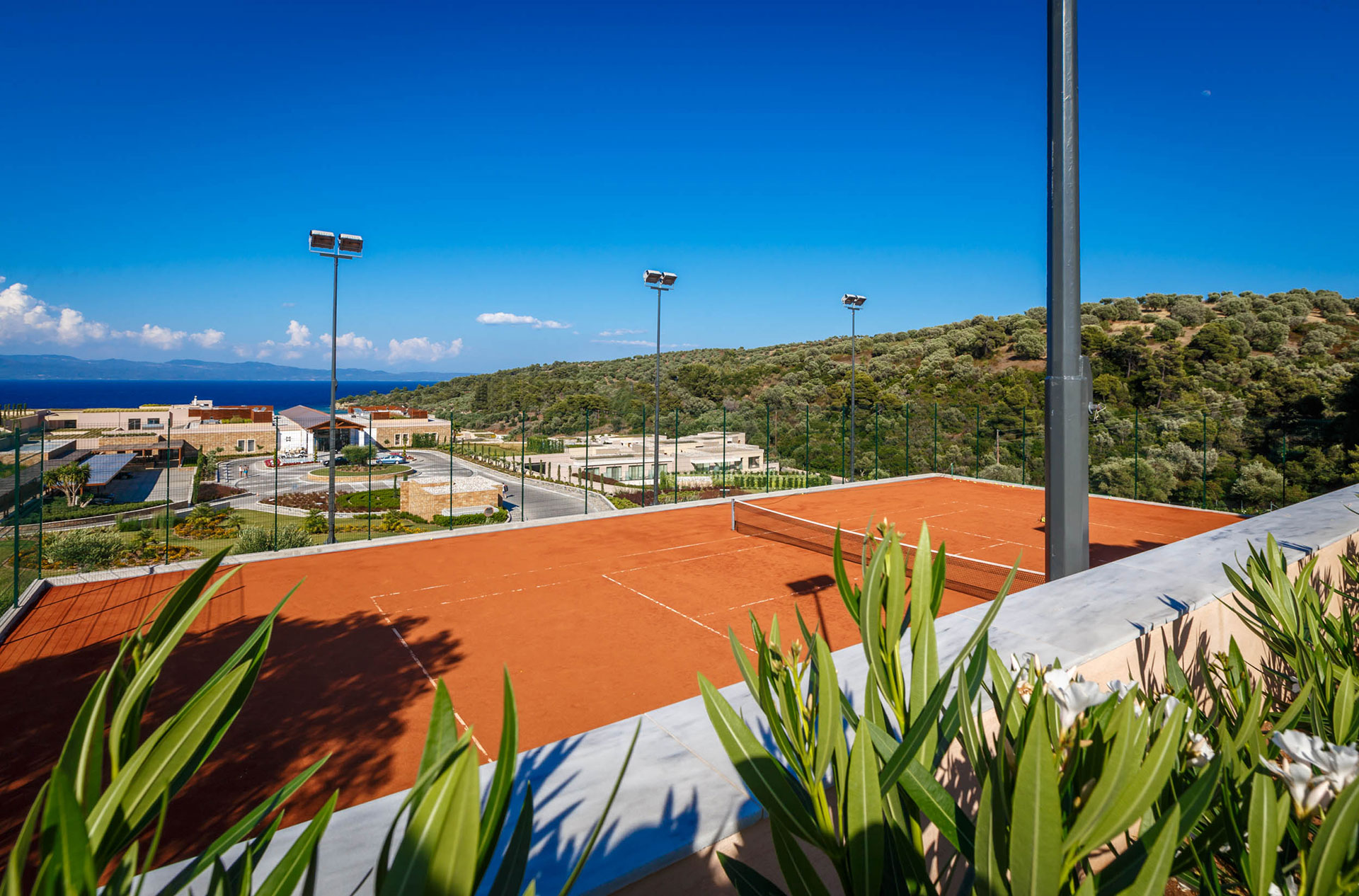 Clay tennis court with panoramic sea and hillside views under a clear blue sky