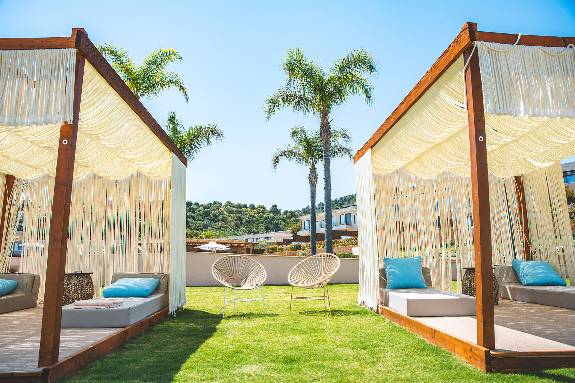 Luxurious cabanas with white draped canopies, blue cushions, and palm trees on a sunny lawn