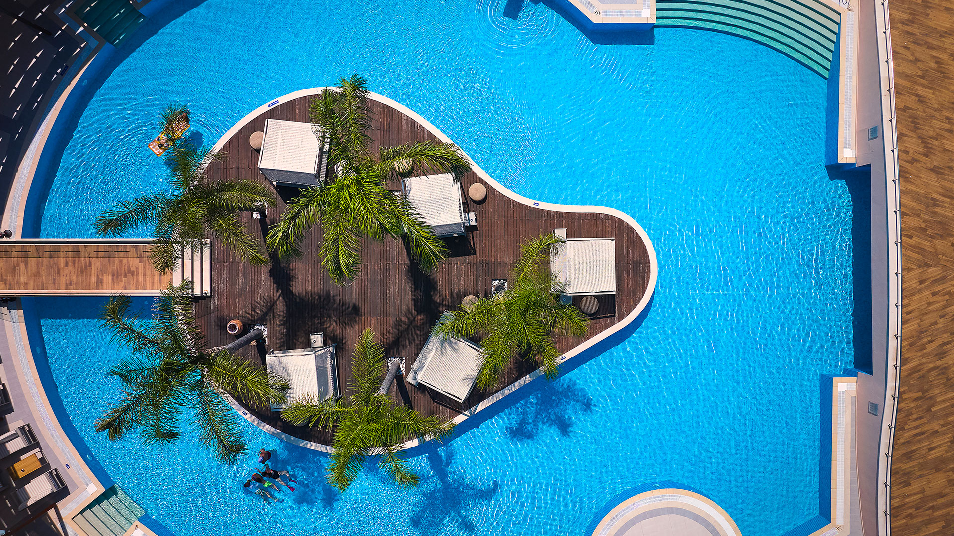 Aerial view of circular pool island with cabanas, palm trees and wooden deck