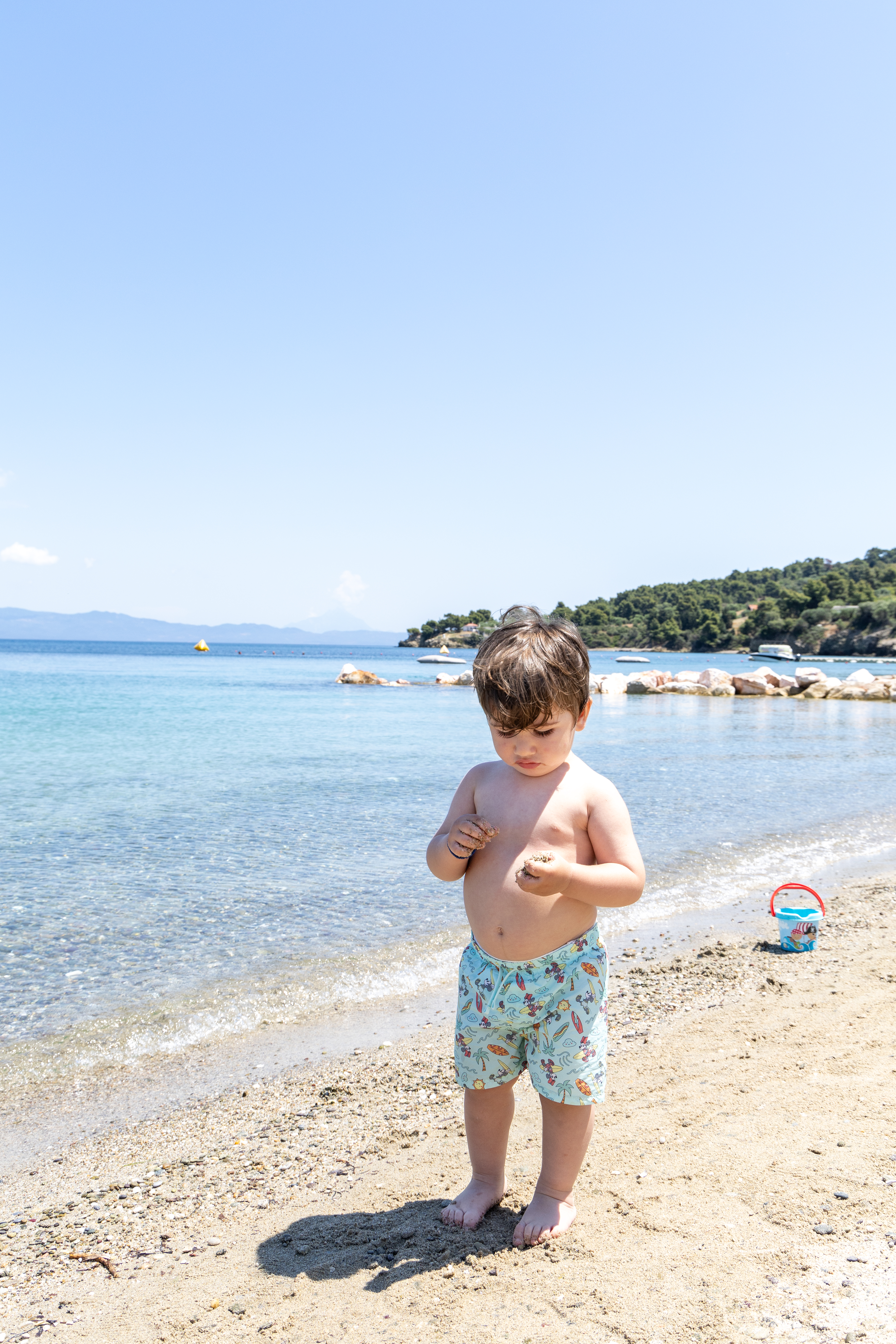 Toddler playing with sand on the golden beach with turquoise sea in the background