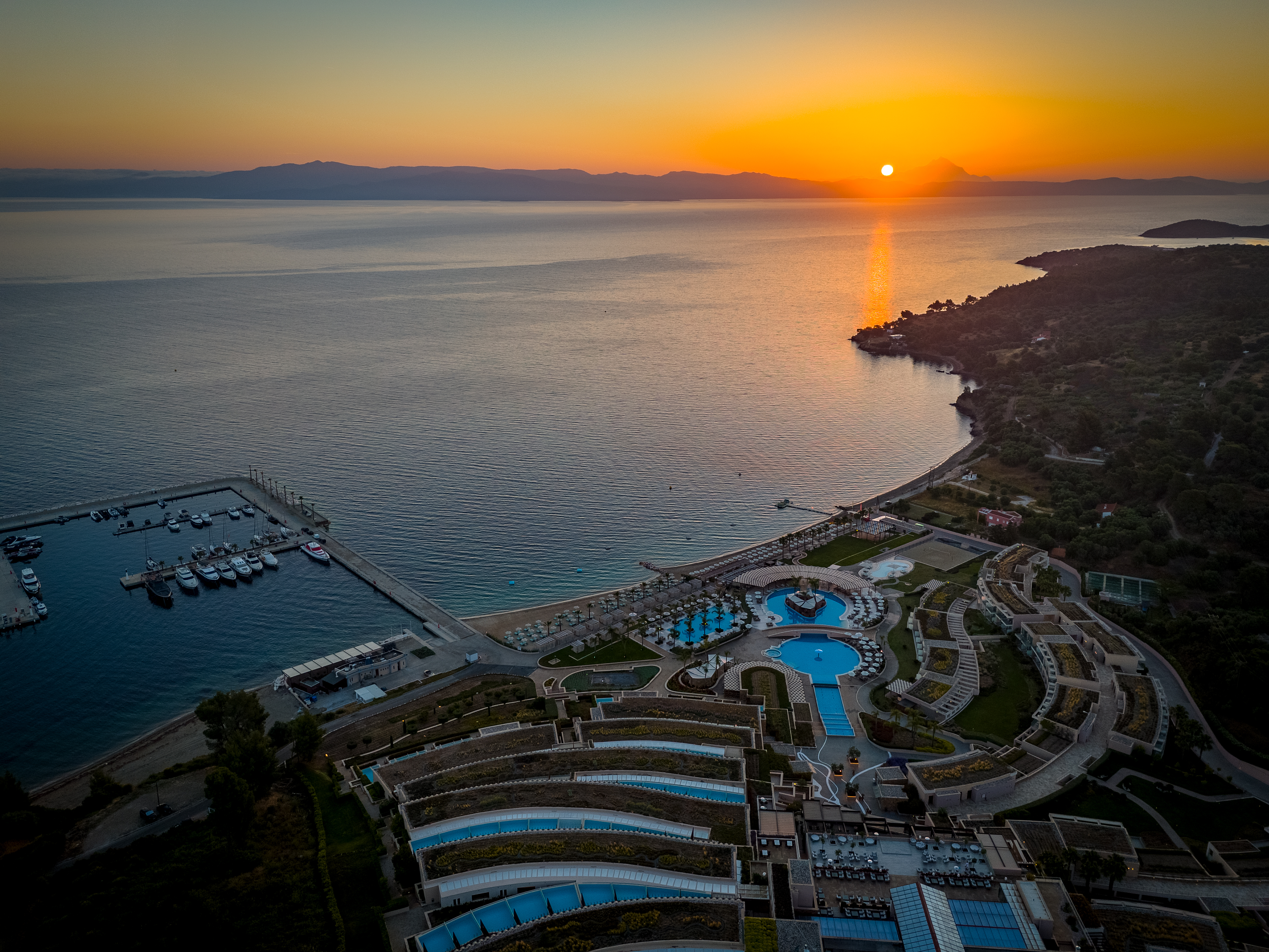 Sunset aerial view of Miraggio Resort with its pools, marina, and coastline glowing under golden evening light