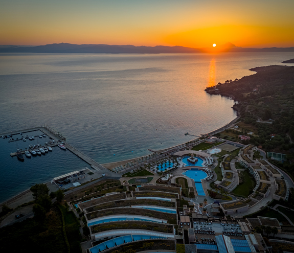 Sunset aerial view of Miraggio Resort with its pools, marina, and coastline glowing under golden evening light
