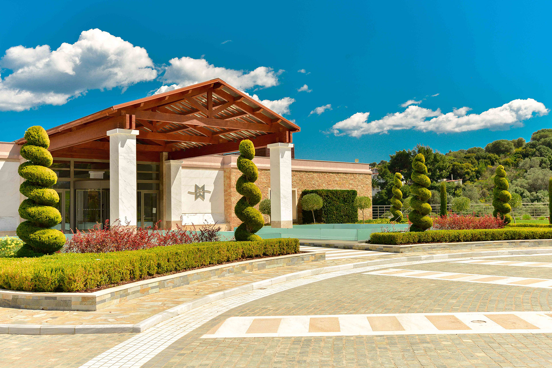 Main entrance with wooden canopy, elegant landscaping, and geometric topiary trees
