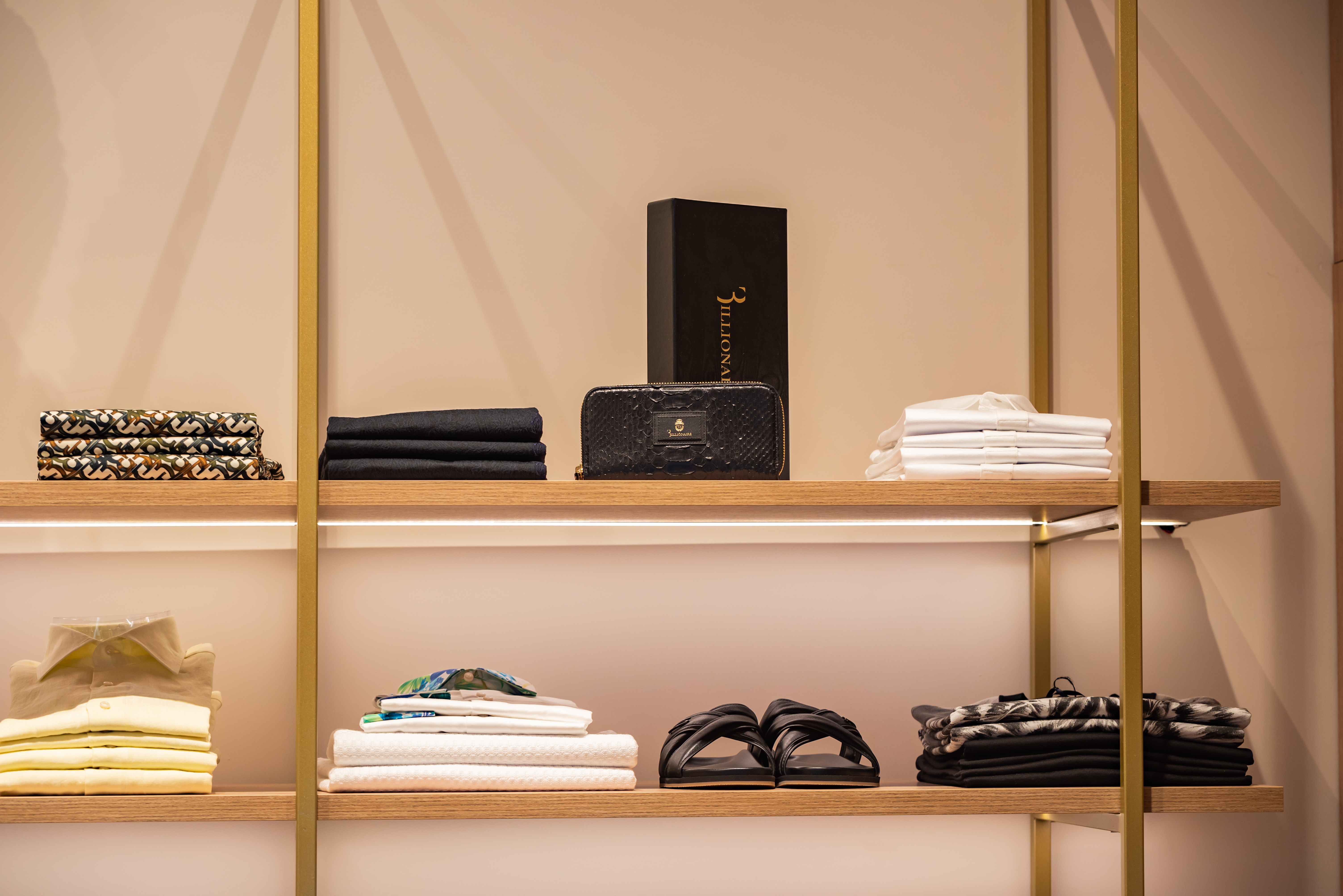 Elegant display of folded men's shirts, leather accessories, and sandals on wooden shelves
