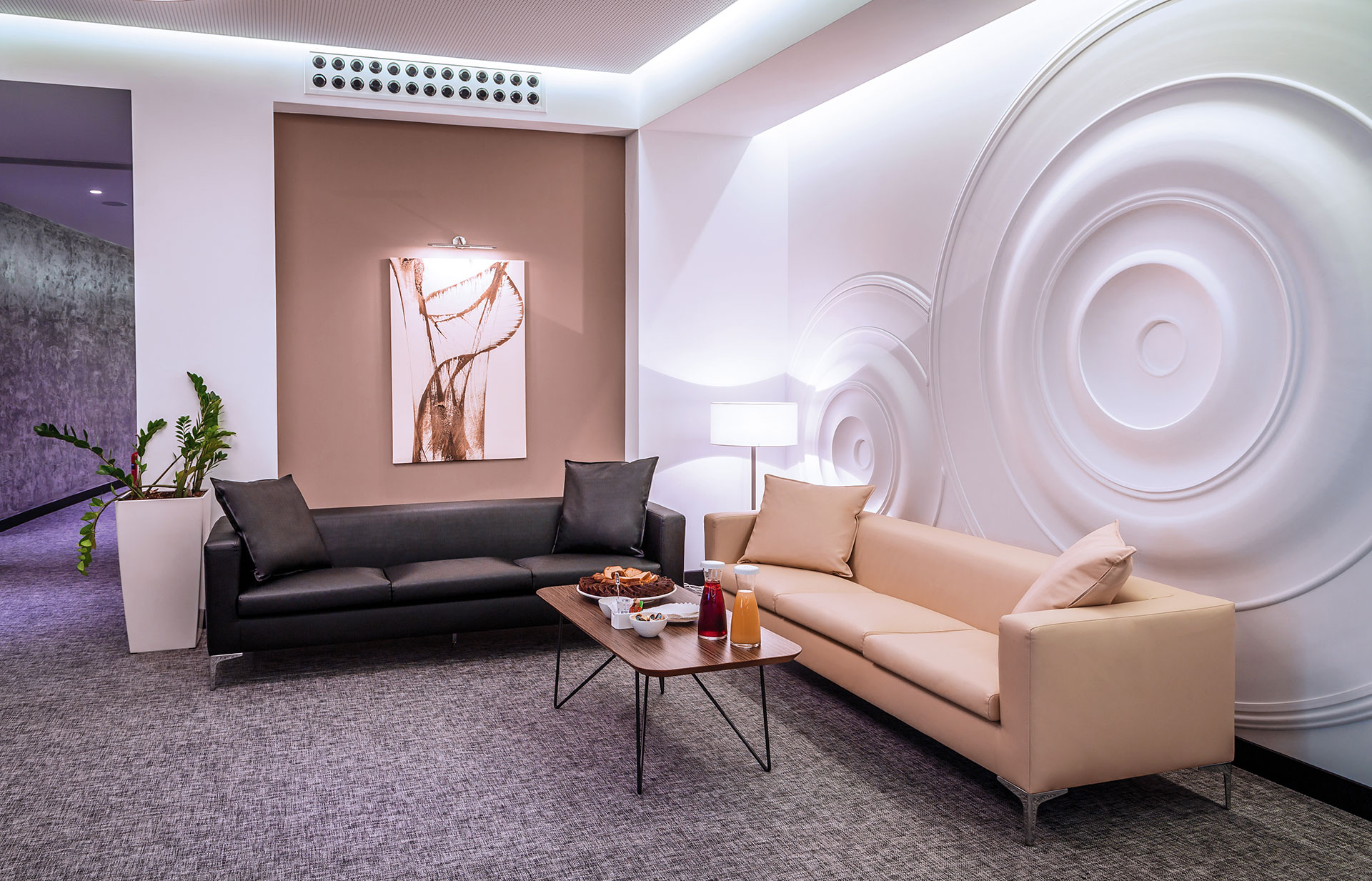 Elegant conference lounge area with modern sofas, decorative wall art, and refreshments setup