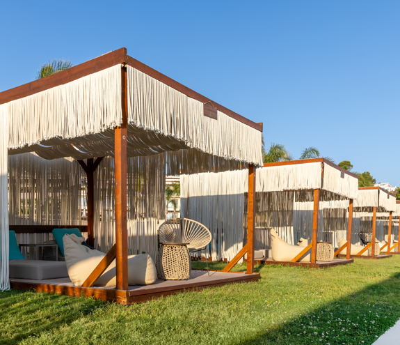 Row of elegant cabanas with fringe curtains, plush loungers, and stylish details under clear blue skies