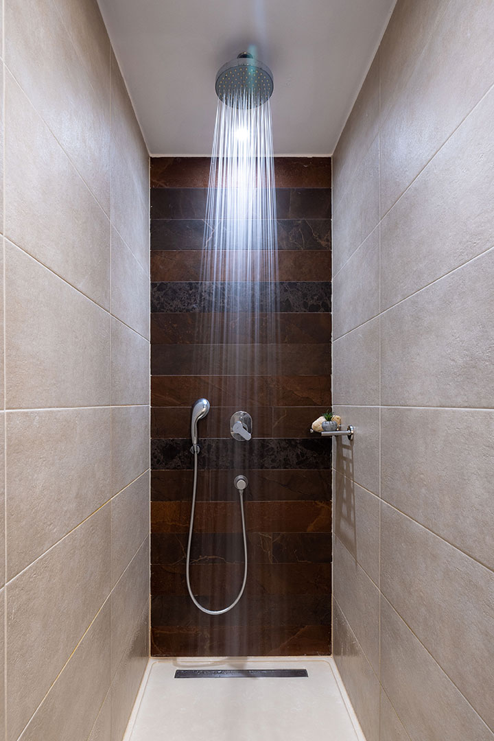 Family room walk in shower with brown marble tiles and modern chrome fixtures