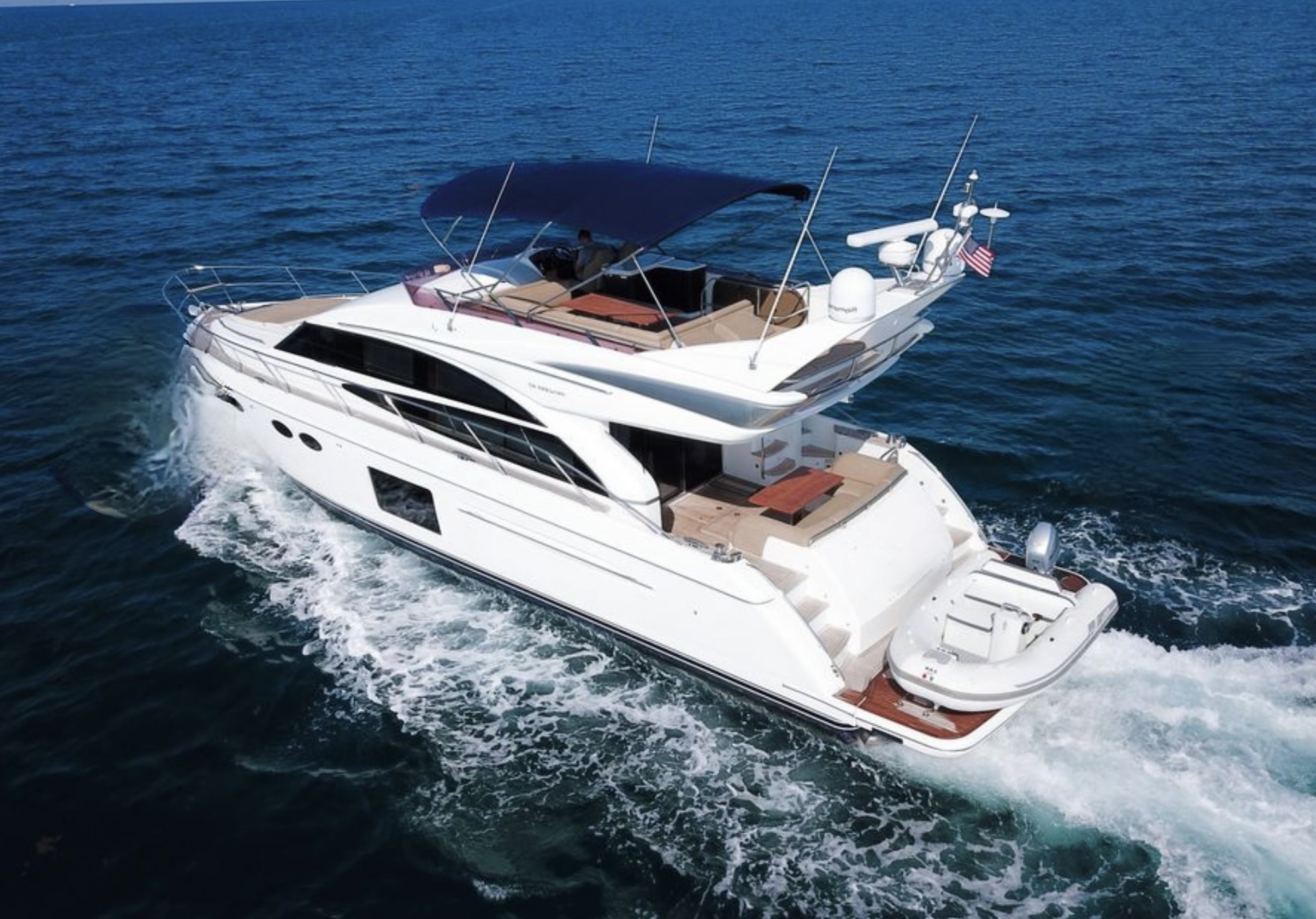Luxury white flybridge yacht cruising on calm blue waters with shaded upper deck and real tender
