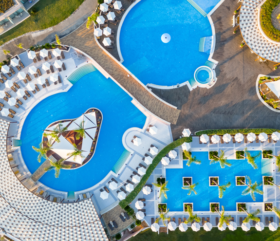 Aerial top-down view of the stunning pool complex with multiple interconnected pools, palm trees and sunbeds 