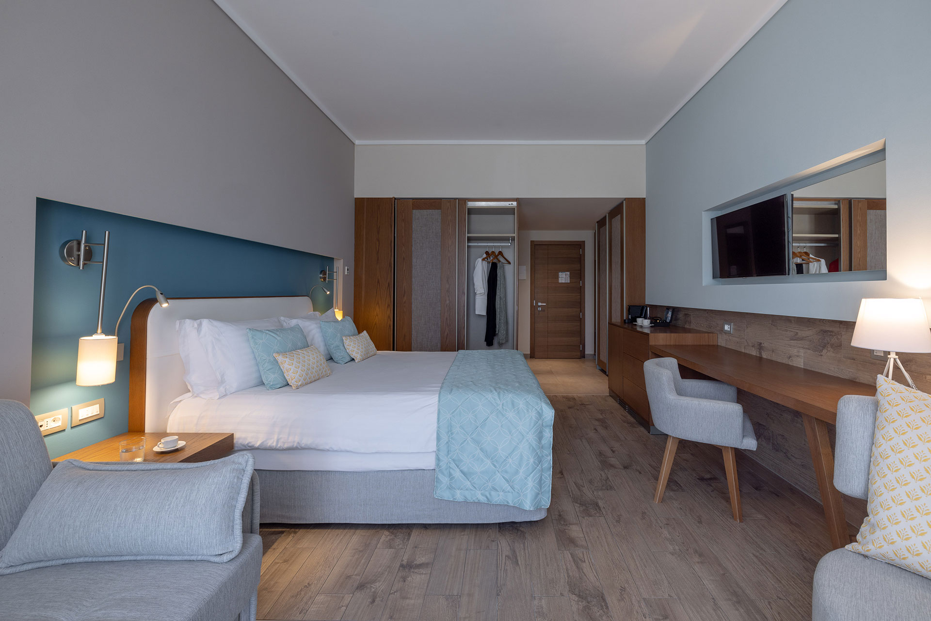 Spacious deluxe room with king bed, wooden floors, work desk, and calming blue interior
