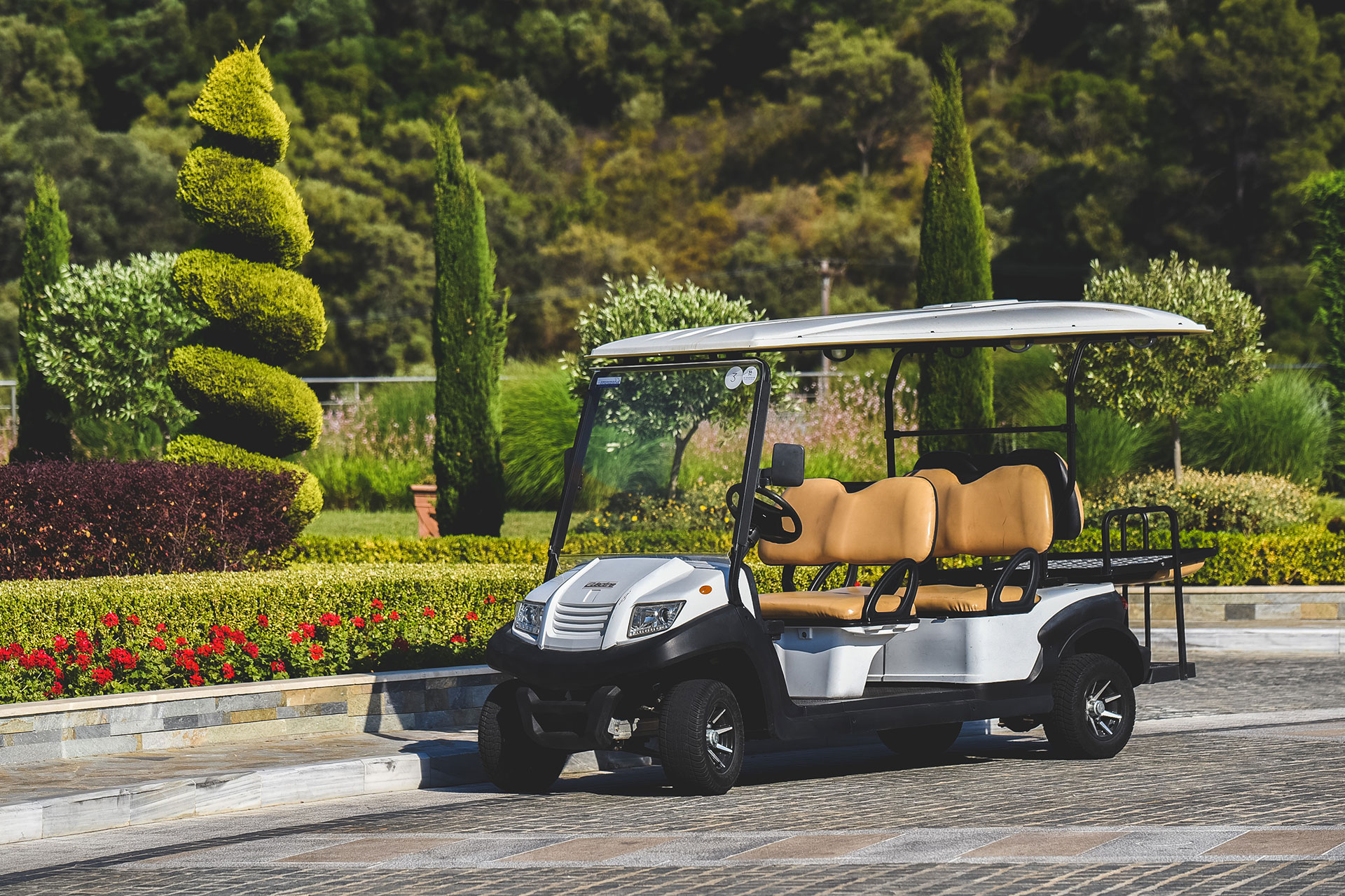 Electric golf cart parked by manicured gardens and lush greenery